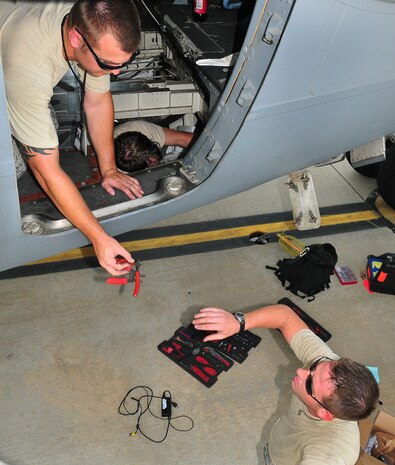 Tech. Sgt. Paul Higgins hands a pair of diagonal cutters and wire strippers to Senior Airman Lane McCoppin while Senior Airman John Theriot Jr. works below the floor of a C-17 on the flightline here Aug. 19. The Airmen worked to remove and replace a corroded power outlet which mates the aircraft to external power during maintenance. Sergeant Higgins and Airman McCoppin are electrical and environmental specialists with the 437th Aircraft Maintenance Squadron, and Airman Theriot is an electrical and environmental specialist with the 315th Aircraft Maintenance Squadron. (Air Force photo/Staff Sgt. Daniel Bowles)