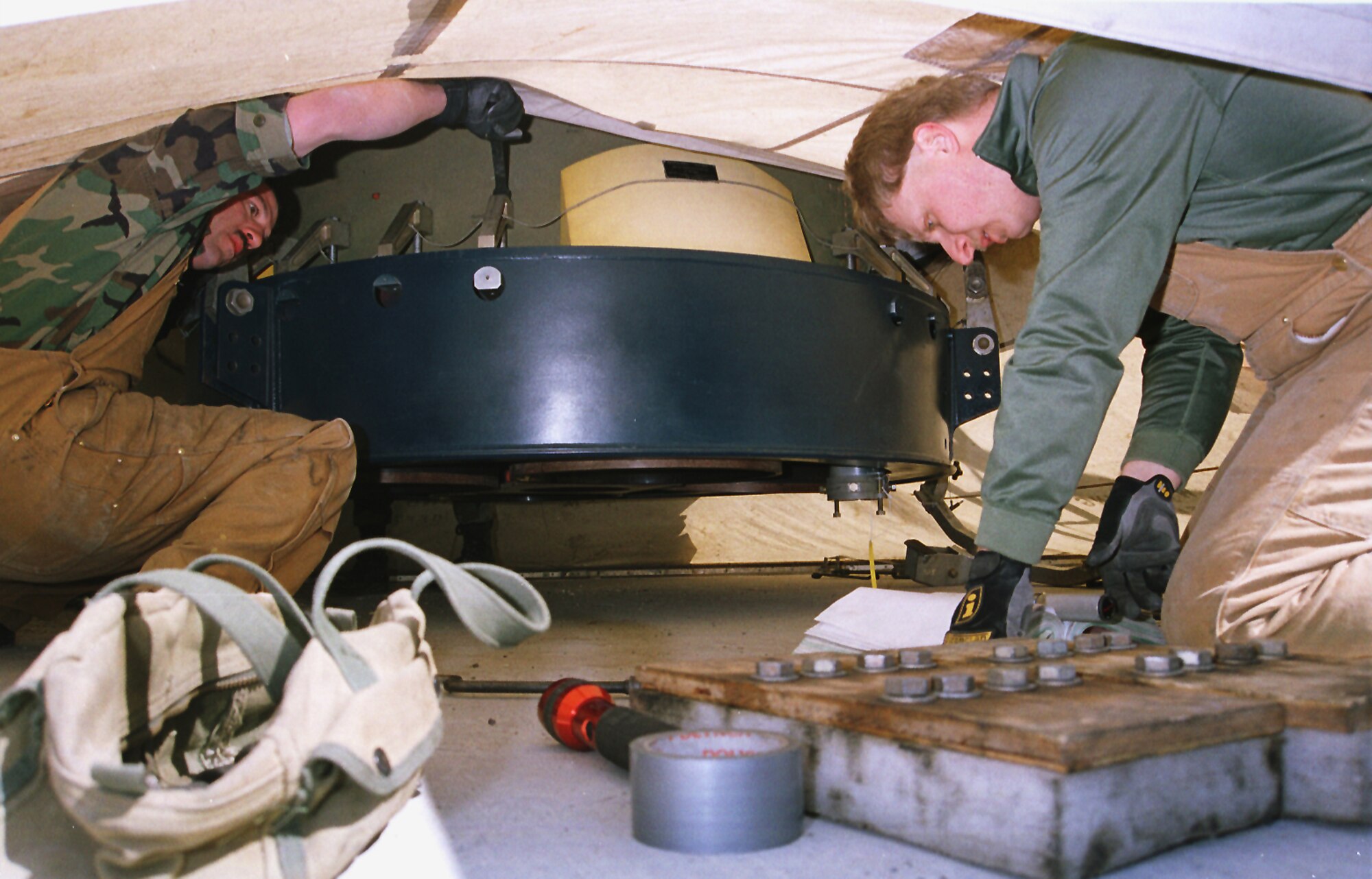 In the narrow space between the top of the launcher closure door and thrust nozzles of a suspended Minuteman III,  Staff Sgts. Jordan Hatch and Dean Phelan, 341st Maintenance Squadron technicians, remove tie-downs to lower the missile into launch facility Hotel-02 April 16, 2001, during the first booster replacement at Malmstrom.  (U.S. Air Force photo/John Turner)