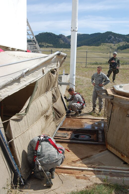 Airman 1st Class Christopher Foster (left) and Senior Airman Joshua Holder (right), 341st Missile Maintenance Squadron missile handling team technicians, set up a frame for an environmental cover used to protect the missile from the elements at launch facility Echo-08 Aug. 18. Airman Brent Schiermann, a maintenance trainee, and Senior Airman Stephen Young, 741st Missile Security Forces Squadron security escort team member, observe the installation of Malmstrom’s 150th Minuteman III solid-propellant replacement booster; extending the service life of the missile through 2020. The first MMIII replacement booster was delivered in April 2001.  (U.S. Air Force photo/Staff Sgt. Eydie Sakura)