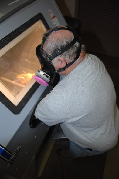 MINOT AIR FORCE BASE, N.D. -- Barry Davis, a corrosion control technician in the 91st Missile Maintenance Squadron, works inside a sand blasting cabinet removing corrosion from a debris bin pin. The corrosion control shop here uses this sand blasting cabinet and other equipment to treat metals and remove corrosion. (U.S. Air Force photo by Staff Sgt. Stacy Moless)