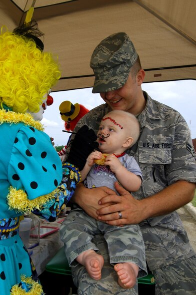 MINOT AIR FORCE BASE, N.D.--Airman 1st Class Edwin Brown, 91st Missile Maintenance Squadron facility maintenance team member hold his son 10-month-old Brody, while “Cloudy” Claudia Gillespie finishes of his mustache during the end of summer block party here Aug. 14.  The annual event featured a car & bike show, games, face painting, prizes, clowns and food for base personnel. (U.S. Air Force photo by Tech. Sgt.  Lee A. Osberry Jr.)
