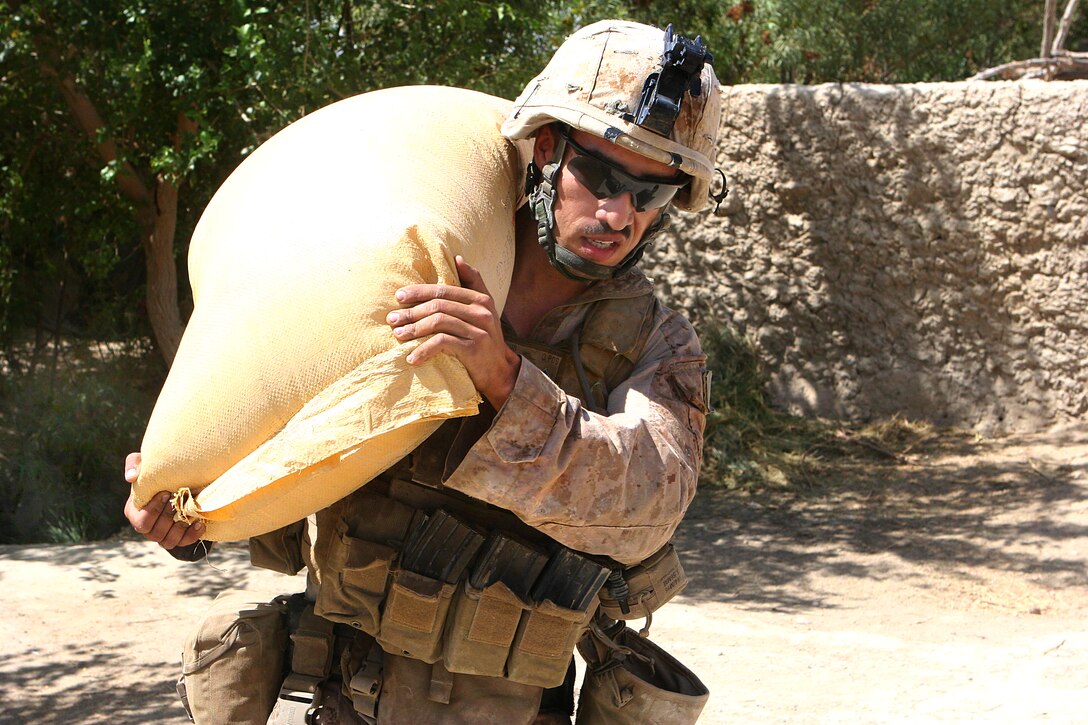 U.S. Marine Corps Cpl. Angelo Agudelo carries a bag of ammonium nitrate from a cache of materials to make improvised explosive devices found in a compound recently occupied by insurgents in Garmsir district in Helmand province, Afghanistan, Aug. 10, 2009. Agudelo is a team leader, assigned to Echo Company, 2nd Battalion, 8th Marine Regiment.