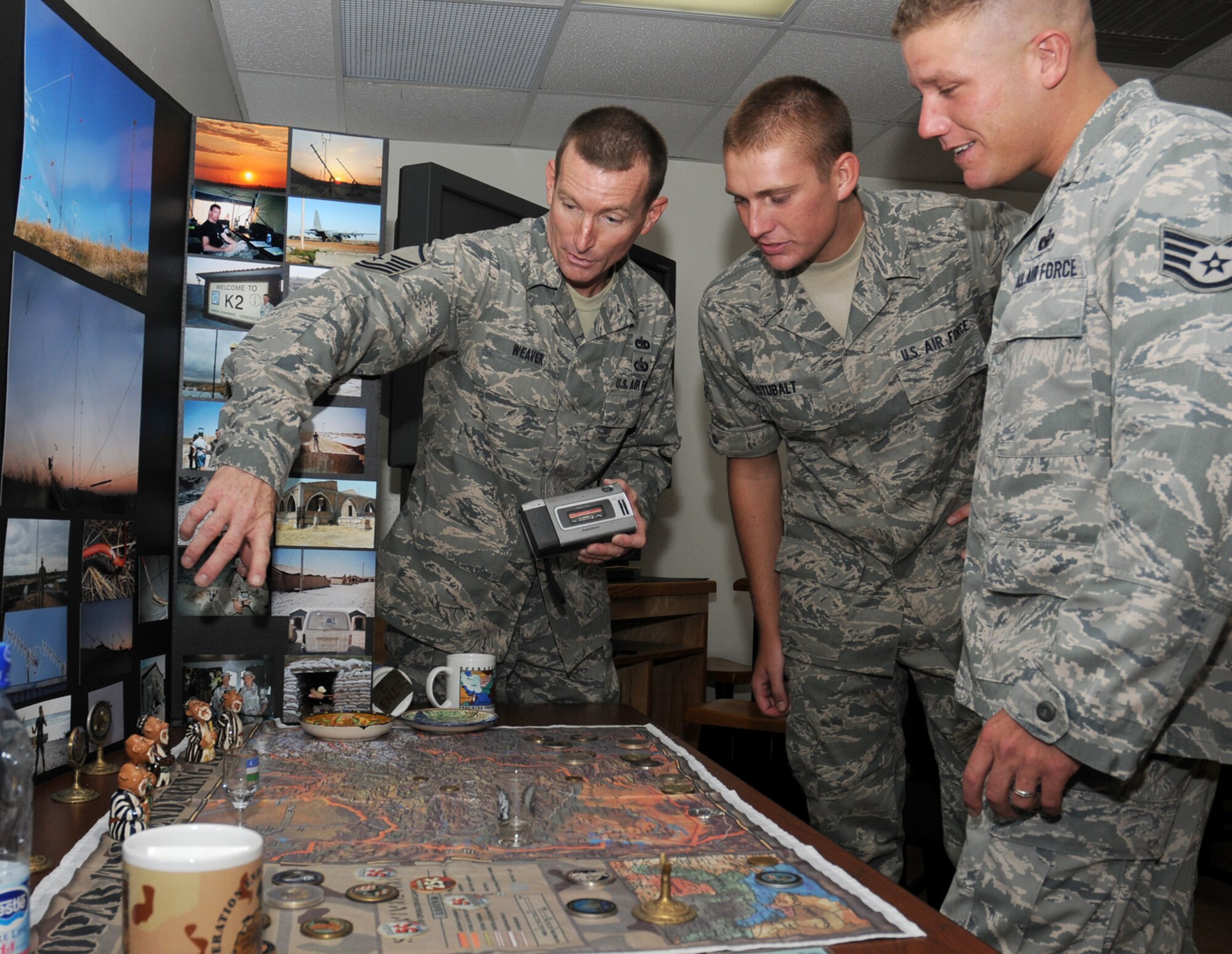 Master Sgt. Michael Weaver, left, shows Airman 1st Class Aaron Stubalt and Staff Sgt. Warren Kerrigan some pictures, posters and collages of radio systems equipment he used while deployed to Camp Stronghold Freedom, Uzbekistan.  All three are students in the 338th Training Squadron’s ground radio maintenance course.  Sergeant Weaver, a 7-level radio systems craftsman and freelance photographer, provided the display to show how the equipment the class is training on is actually used in a tactical operations environment.  Sergeant Weaver, who’s stationed at Duke Field, Fla., is taking the course to retrain after his previous Air Force Specialty Code was eliminated.  (U.S. Air Force photo by Kemberly Groue)