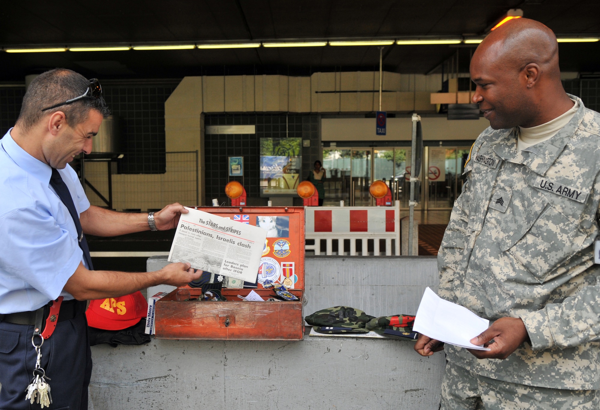 Stephen Syring (left), Frankfurt Airport Rescue and Fire Service aircraft rescue and firefighter instructor, displays a news paper from 1996, as U.S. Army Sgt. Deon Washington, U.S. Forces Customs Europe senior customs agent, watches, Aug. 18, 2009, Frankfurt Airport, Germany. The time capsule was found during construction for cargo buildings for the Frankfurt Airport. (U.S. Air Force photo by Senior Airman Nathan Lipscomb)