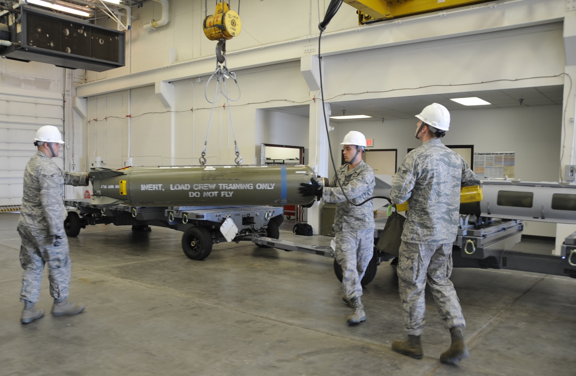(Left to right) Airman 1st Class Michael DiRienzo, Airman John Baker and Airman 1st Class David Benner, 28th Munitions Squadron conventional maintenance crew members, work together to lift a Cluster Bomb Unit-87 here, August 20.  The CBU-87 is a 900-pound bomb that, after being dropped, will deploy several smaller bomblets over an area. (U.S Air Force photo/Airman 1st Class Anthony Sanchelli)