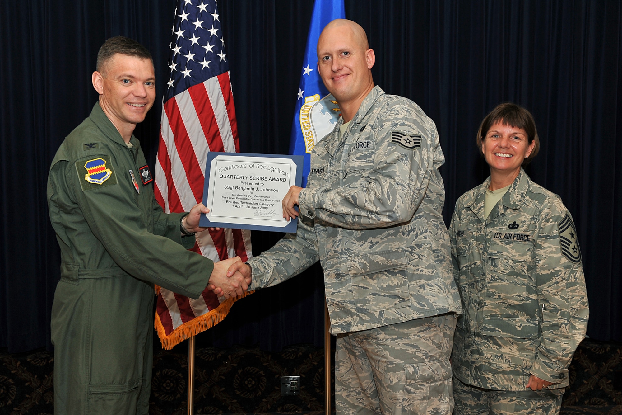 OFFUTT AIR FORCE BASE, Neb. -- Col. John T. Rauch, 55th Wing vice commander, presents Staff Sgt. Benjamin J. Johnson, 55th Operations Group, with the scribe award for the enlisted Non-commissioned officer category as Chief Master Sgt. Lisa A. Sirois, 55th Wing command chief, looks on during the second quarter scribe awards luncheon at the Patriot Club Aug. 12. U.S. Air Force Photo by Charles Haymond
