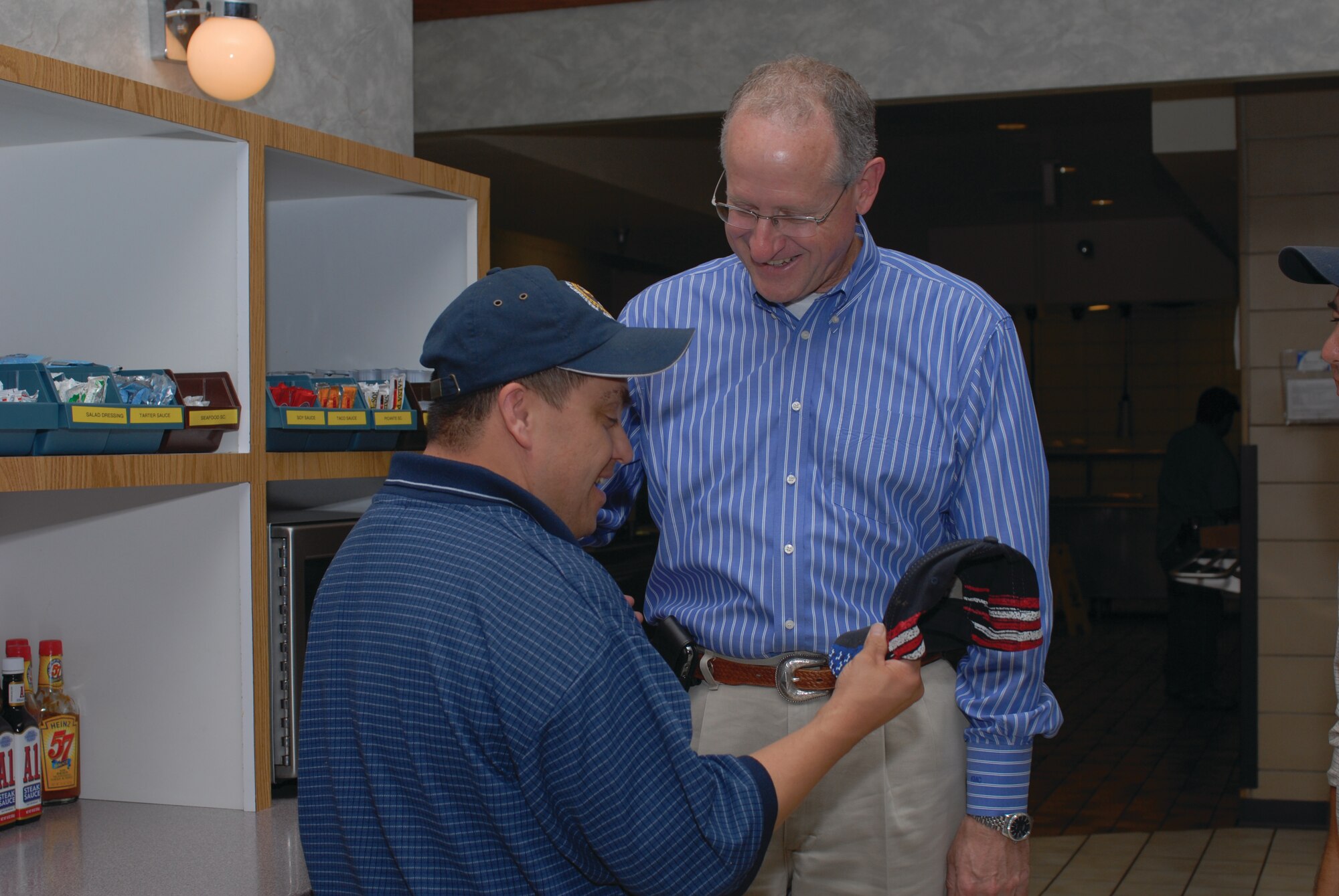 Ricky Bonilla, Western Winds Dining Facility staff worker, shows Congressman Mike Conaway, 11th District of Texas, his hat that he received for employee of the month at the dining facility, Aug. 4. (U.S. Air Force photo by Staff Sgt. Laura R. McFarlane)