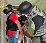 Airman 1st Class Aaron Zelenka is released from handcuffs by Pfc. Roger Medlock after a training scenario with the Summerville Emergency Services Unit at a vacant home on East Jackson Drive here Aug. 21. Airman Zelenka was apprehended as an aggressor after simulated munitions were fired in the use of force training scenario. Airman Zelenka is an entry controller with the 437th Security Forces Squadron and Medlock is a traffic division motorcycle officer with the Summerville Emergency Services Unit. (U.S. Air Force photo/Staff Sgt. Daniel Bowles)