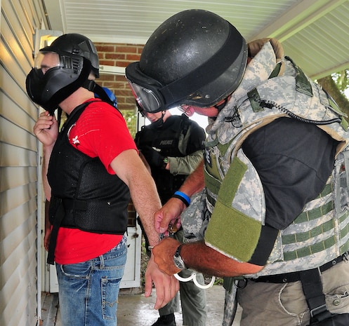 Airman 1st Class Aaron Zelenka is released from handcuffs by Pfc. Roger Medlock after a training scenario with the Summerville Emergency Services Unit at a vacant home on East Jackson Drive here Aug. 21. Airman Zelenka was apprehended as an aggressor after simulated munitions were fired in the use of force training scenario. Airman Zelenka is an entry controller with the 437th Security Forces Squadron and Medlock is a traffic division motorcycle officer with the Summerville Emergency Services Unit. (U.S. Air Force photo/Staff Sgt. Daniel Bowles)