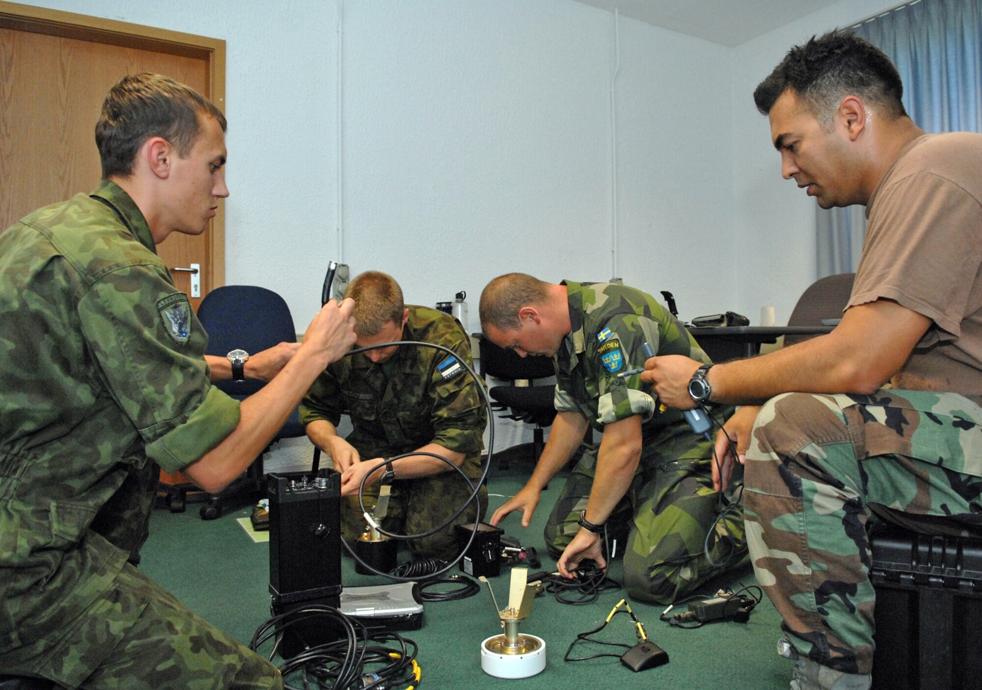Tech. Sgt. Nicholas Picoc (right), who is in charge of training and evaluations at the U.S. Air Forces in Europe Air Ground Operations School, assists international forward air controllers with the assembly of the ROVER III, a kit which mainly consists of a tactical laptop, antennas, cables and other items used to receive live video feed from aircraft during close-air-support operations. Two Estonian air force members and a Swedish army ranger spent a week in pre-deployment briefings, computer simulation, and field training prior to deployment thanks to the joint efforts of the staff at the USAFE AGOS and the International Security Assistance Force Cell at NATO Allied Air Component Command Headquarters Ramstein Aug. 17- 21. (U.S. Air Force photo/Master Sgt. Corey Clements) 