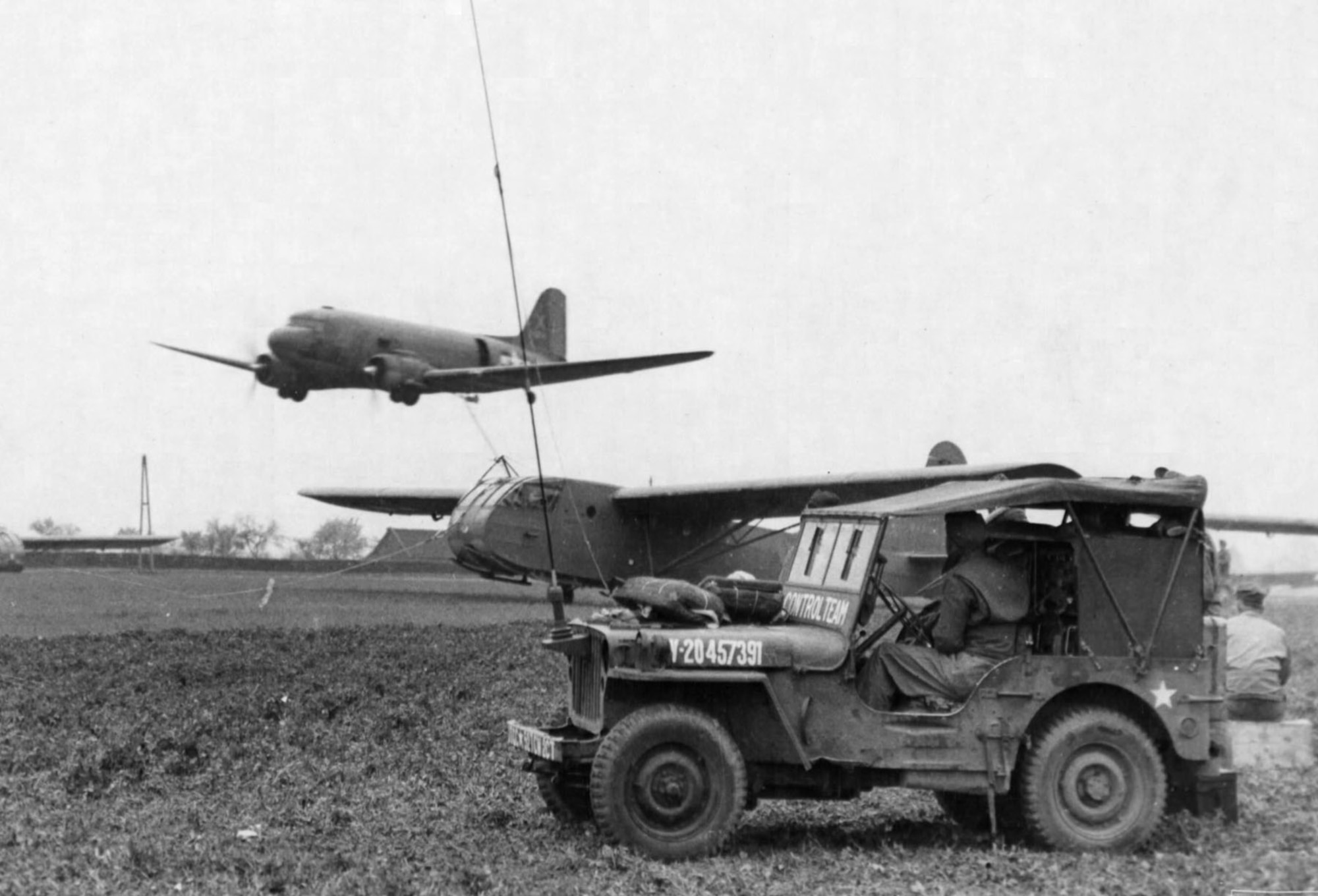 Making a low pass over the field, the C-47 has its hook dropped to snatch the CG-4 glider as controllers watch from their jeep. (U.S. Air Force photo)