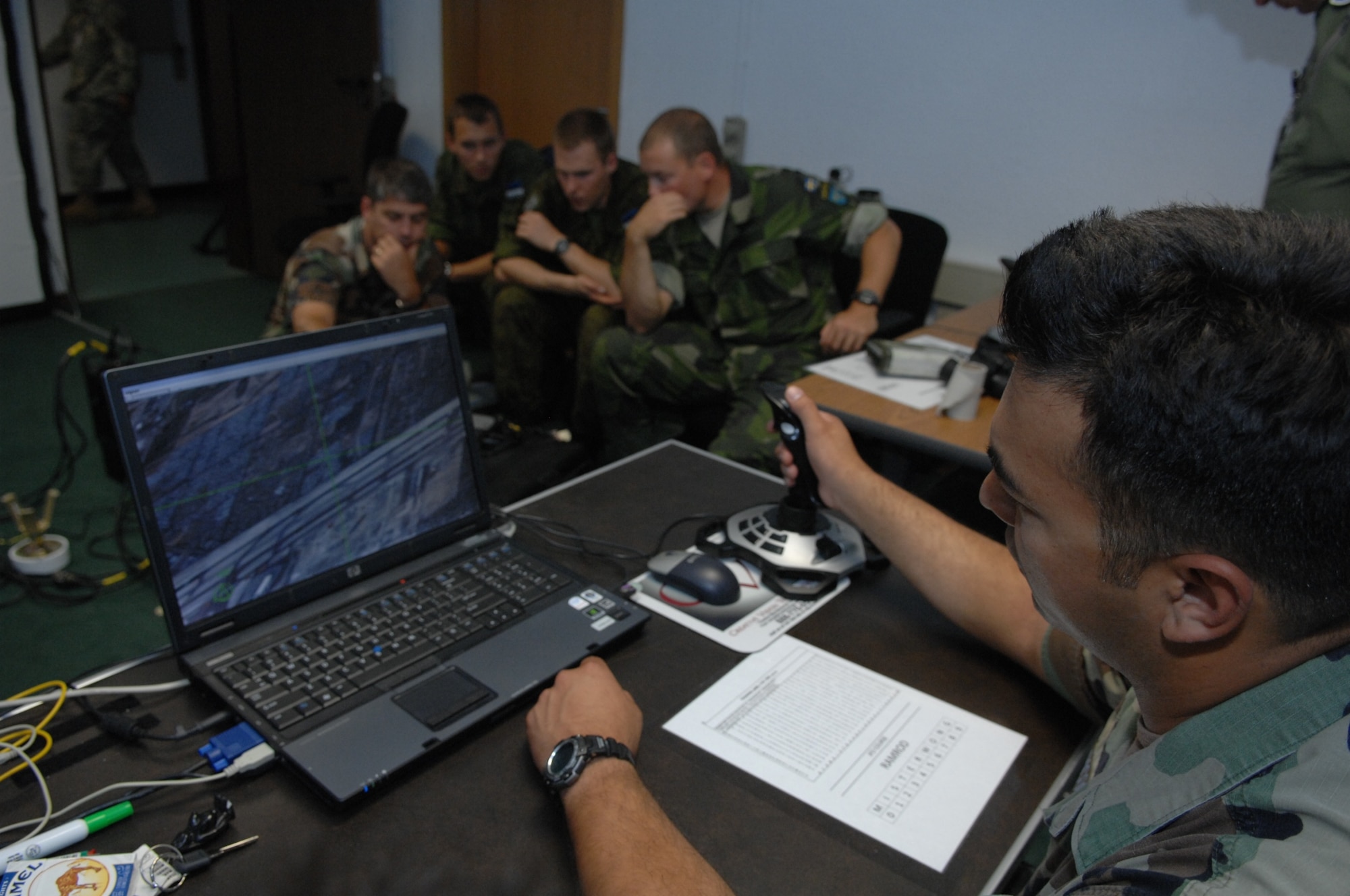 RAMSTEIN AIR BASE, Germany- Tech. Sgt. Nicholas Picoc (right), who is in charge of training and evaluations at the U.S. Air Forces in Europe Air Ground Operations School, operates the aircraft module of a computer simulator for practicing air strikes during close air support operations while  international forward air controllers work the ROVER III, a kit which mainly consists of a tactical laptop, antennas, cables and other items designed to receive live video feed from aircraft.  Two Estonian air force members and a Swedish army ranger spent a week in pre-deployment briefings, computer simulation, and field training prior to deployment thanks to the joint efforts of the staff at the USAFE AGOS and the International Security Assistance Force Cell at NATO Allied Air Component Command Headquarters Ramstein Aug. 17- 21. (U.S. Air Force photo/Master Sgt. Corey Clements)
