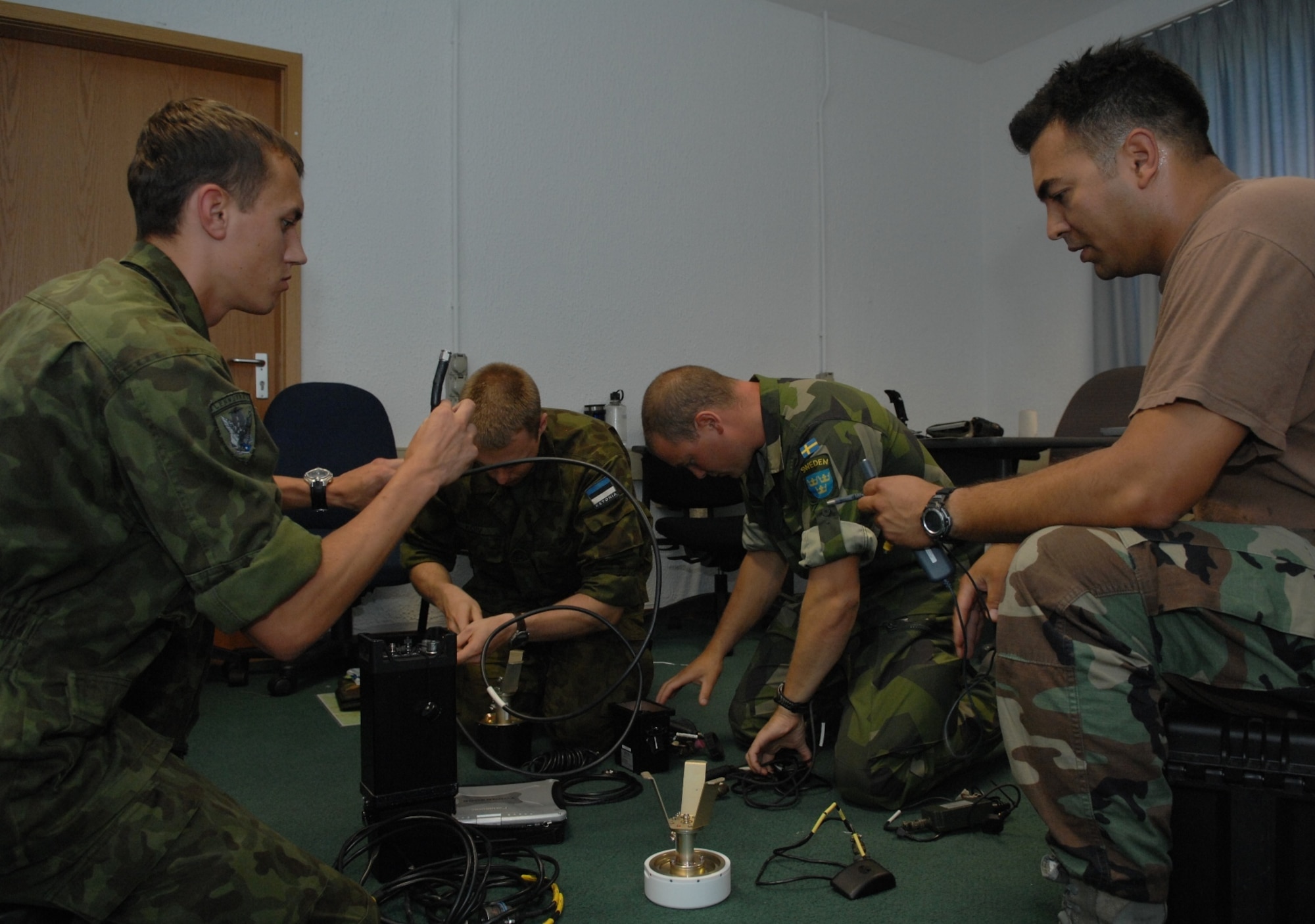 RAMSTEIN AIR BASE, Germany- Tech. Sgt. Nicholas Picoc (right), who is in charge of training and evaluations at the U.S. Air Forces in Europe Air Ground Operations School, assists international forward air controllers with the assembly of the ROVER III, a kit which mainly consists of a tactical laptop, antennas, cables and other items used to receive live video feed from aircraft during close air support operations.  Two Estonian air force members and a Swedish army ranger spent a week in pre-deployment briefings, computer simulation, and field training prior to deployment thanks to the joint efforts of the staff at the USAFE AGOS and the International Security Assistance Force Cell at NATO Allied Air Component Command Headquarters Ramstein Aug. 17- 21. (U.S. Air Force photo/Master Sgt. Corey Clements)