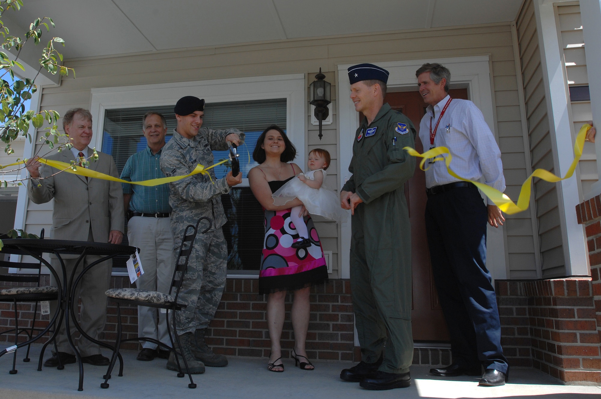 WHITEMAN AIR FORCE BASE, Mo. - Airman 1st Class Joseph Robin, 509th Bomb Wing Security Forces Squadron, cuts the ribbon in front of his new home on Vosler Avenue in the Bear Lake subdivision. Joining in the ceremony (from left to right) was Dan Walsh, president of Walsh Construction, Ken Nugent, 509th Civil Engineering Squadron, Molly and Charli Robin, wife and daughter of Airman Robin, Brig. Gen. Robert Wheeler, 509th Bomb Wing commander, and a member of the Walsh Team. (U.S. Air Force photo/Senior Airman Kenny Holston)

