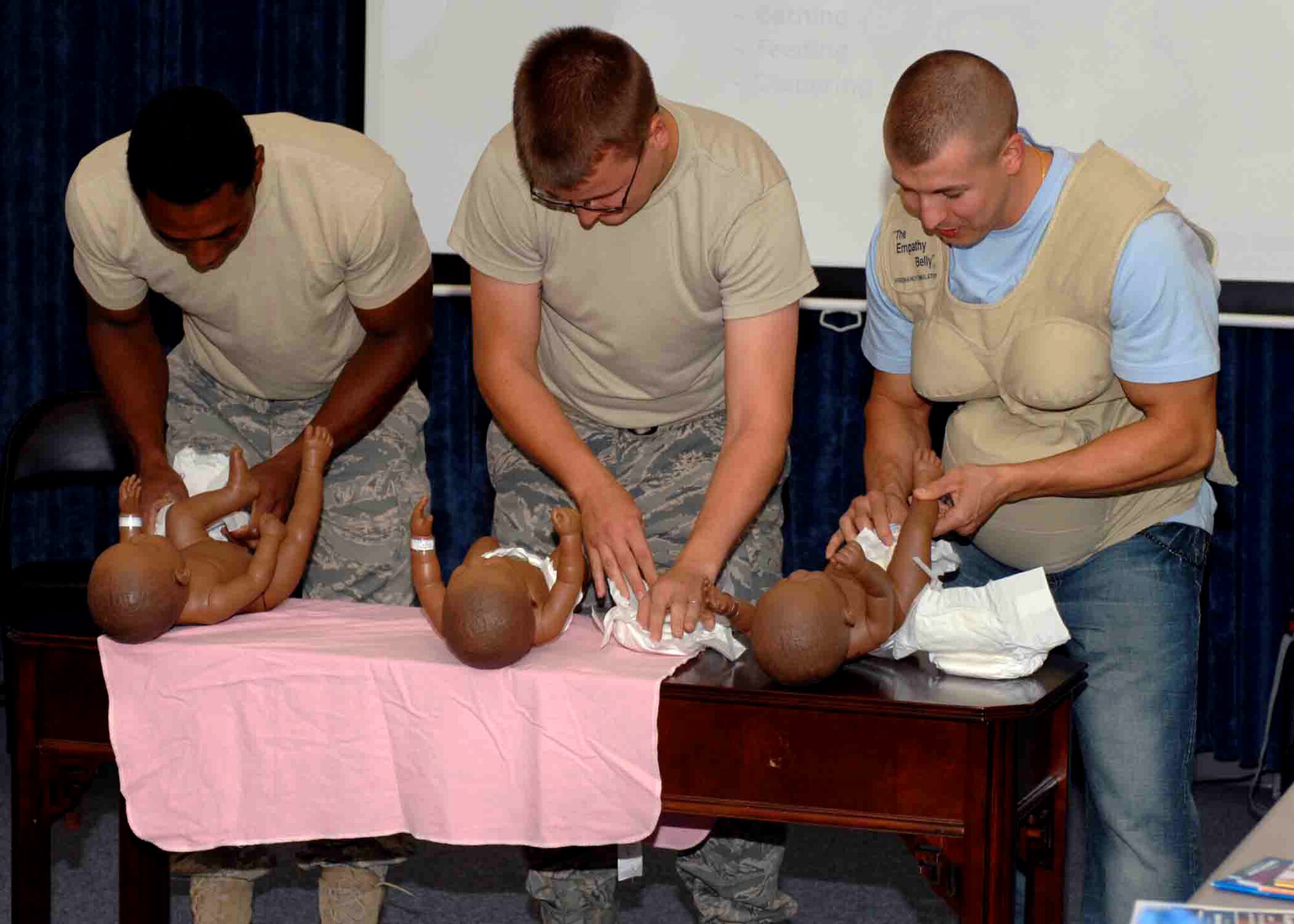 CANNON AIR FORCE BASE, N.M.-- (Left to right) Staff Sgt. Dontaevious Barber, 27th Special Operations Civil Engineer Squadron, Airman 1st Class Elijah Wootten, 27th Special Operations Component Maintenance Squadron, and Senior Airman Ray Schatz, 27th Special Operations Medical Dental Group, compete in a diaper-changing contest in the medical clinic Aug. 25.  Dad's 101 Class is hosted by the Family Advocacy Office on Cannon. Airman Shaz is wearing an Empathy Belly suit that simulates some of what expectant mothers experience. To sign up for the next class, call 784-2474.  (U.S. Air Force photo by Airman 1st Class James Bell) 