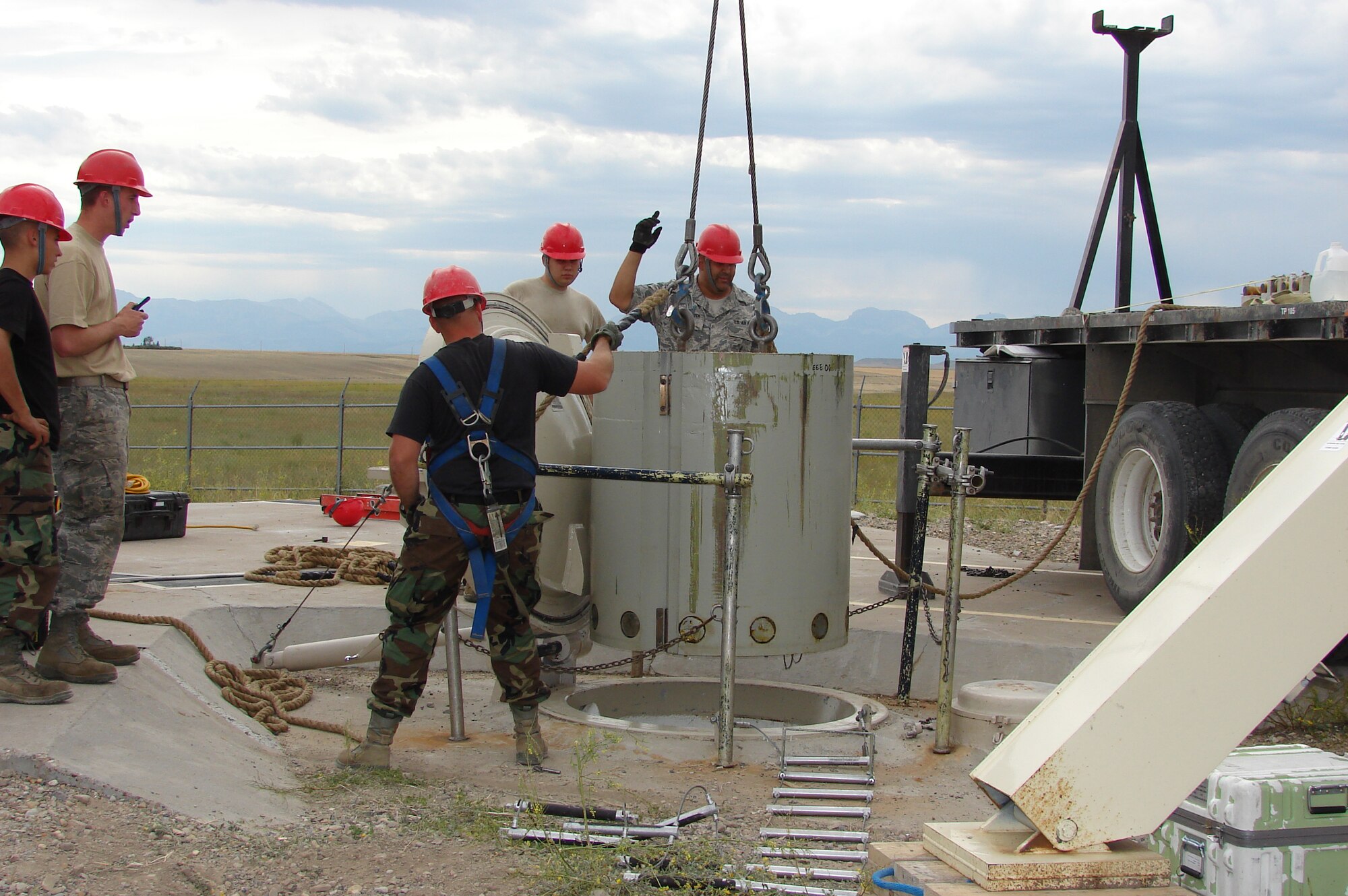 Tech. Sgt. Ben Vandermissen, 341st Missile Maintenance Squadron electro-mechanical team critical tasks supervisor, directs a crane operator Aug. 23, as Senior Airman Shawn Scrivener, 341st MMXS EMT team chief, mans the guide rope as a 14,000 pound secondary door is hoisted out of the personnel access hatch at Launch Facility T-46. Senior Airman William Johnson, (far back) Airmen 1st Class Garrett Clark (holding radio) and Phillip Smith, also from the 341st MMXS, stand by to assist if needed. (U.S. Air Force photo/Capt. Franklin Adams) 