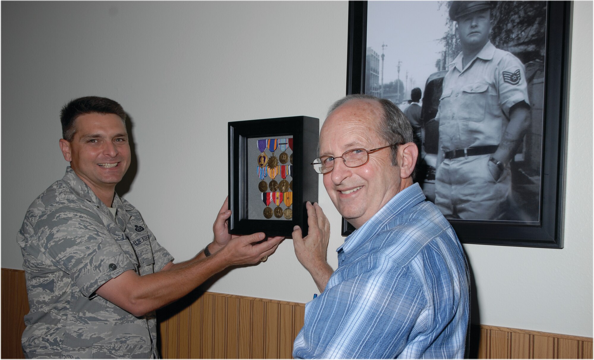 Lt. Col. Erick Lawson, 316th Training Squadron commander, and retired Chief Master Sgt. Ed Bendinelli, vice president, Heritage Chapter, Freedom Through Vigilance Association place a shadow box holding Tech. Sgt. Fred Sebers' medals on the wall near the entrance to Sebers Hall. Tech. Sgt. Sebers' picture is in the background. (U.S. Air Force photo/Lou Czarnecki)
