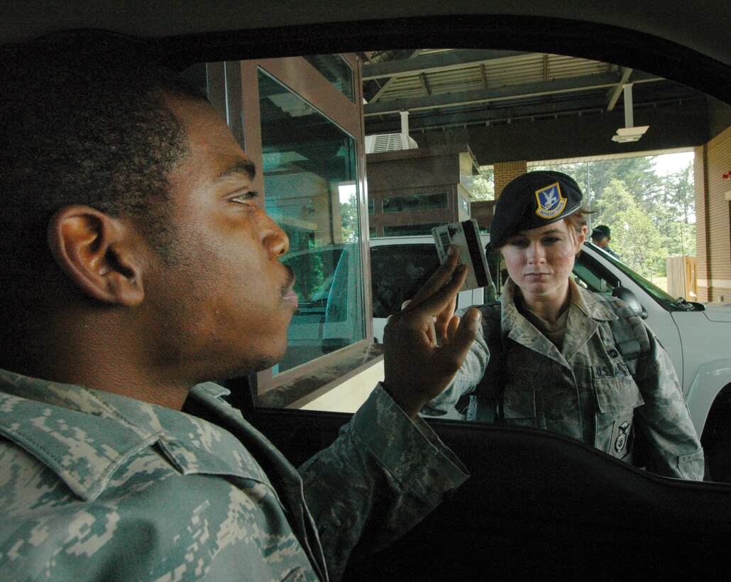 Airman 1st Class Kathleen Lyons, 316th Security Forces Squadron Main Gate entry controller, simulates identification card check of fellow squadron member, Senior Airman Marcus Macon, 316 SFS response team leader through the window Wednesday. In the event of an H1N1 outbreak, security forces at Andrews entry gates would check IDs through closed vehicle windows to prevent the spread of the virus. (U.S. Air Force photo/ Bobby Jones)