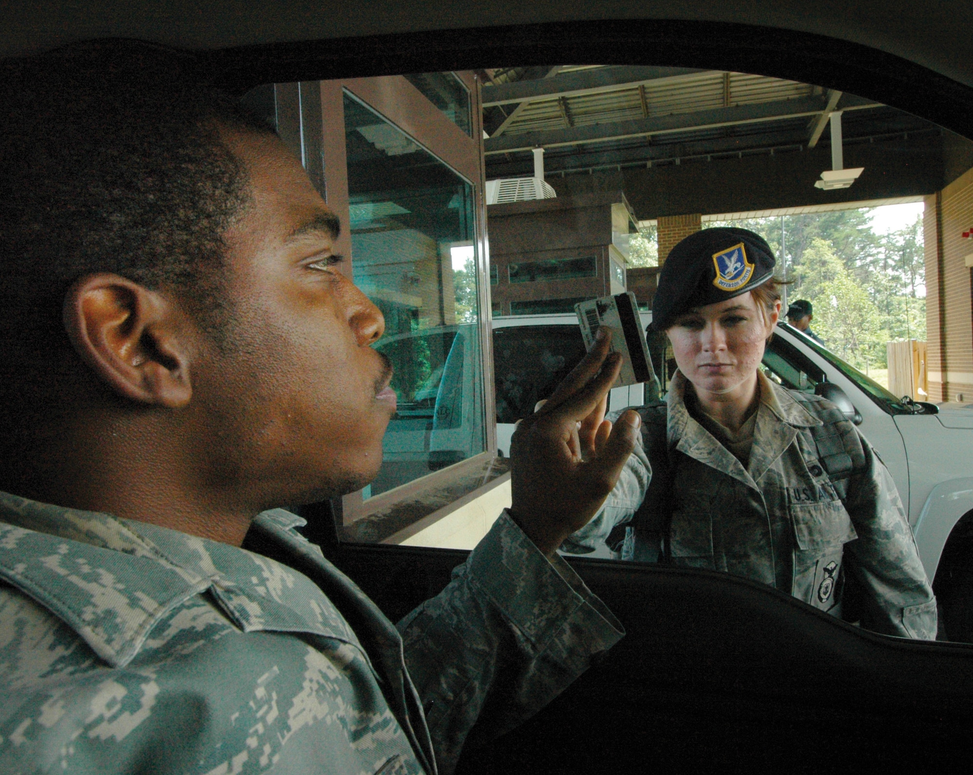 Airman 1st Class Kathleen Lyons, 316th Security Forces Squadron Main Gate entry controller, simulates identification card check of fellow squadron member, Senior Airman Marcus Macon, 316 SFS response team leader through the window Wednesday. In the event of an H1N1 outbreak, security forces at Andrews entry gates would check IDs through closed vehicle windows to prevent the spread of the virus. (U.S. Air Force photo/ Bobby Jones)