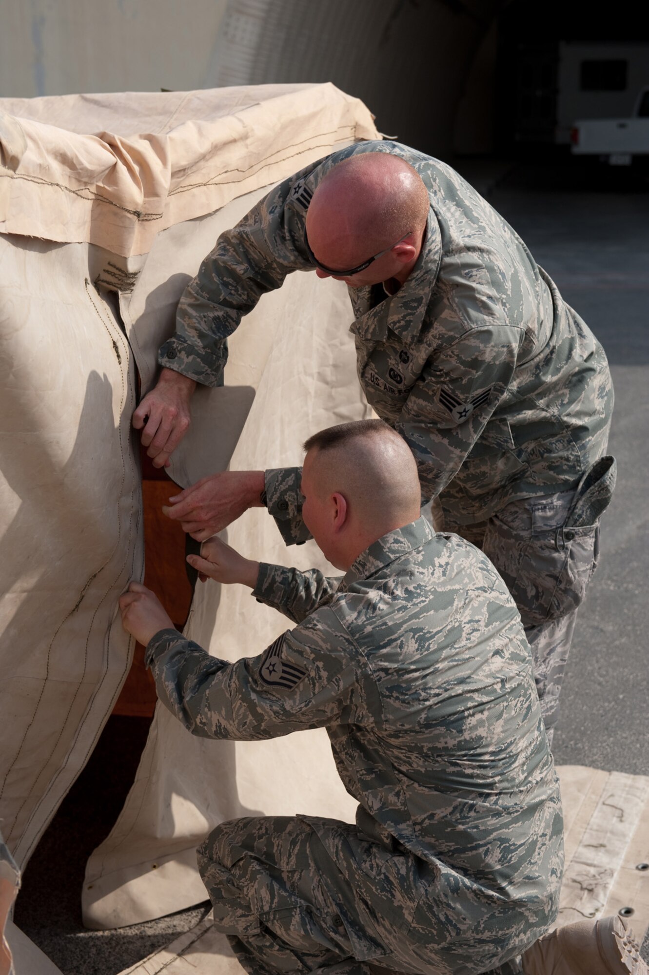Front, Staff Sgt. Delray Sexton and Senior Airman Shane Shanton, 379th Expeditionary Operations Support Squadron aircrew flight equipment personnel, assemble a custom tent, Aug. 22, in Southwest Asia. The tent is designed to provide shade and respite for flightline maintainers during work-rest cycles in extreme temperatures. Sergeant Sexton is a native of Miami, Fla., and deployed from Holloman Air Force Base, N.M. Airman Shanton is a native of Jackson, Ohio and deployed from Kirtland AFB, N.M. Both servicemembers are deployed in support of Operations Iraqi and Enduring Freedom. (U.S. Air Force Photo/ Staff Sgt. Robert Barney) 