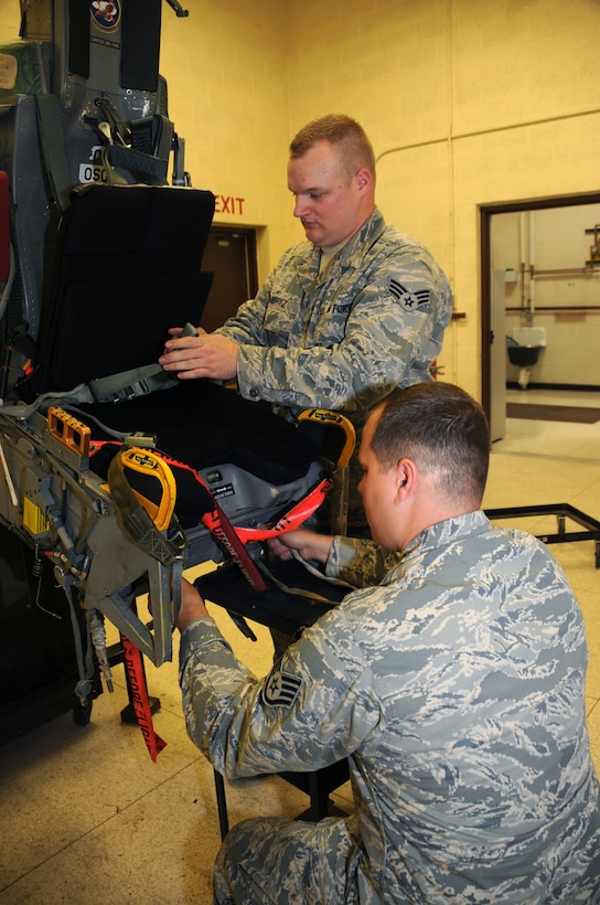 (Left to right) Senior Airman Josh Mertz and Staff Sgt. Don Mings, 28th Maintenance Squadron aircrew egress systems journeymen, install an arm strap assembly on an advanced concept ejection seat II, here, August 27.  Egress Airmen ensure the ACES II works safely and efficiently. (U.S Air Force photo/Airman 1st Class Anthony Sanchelli)