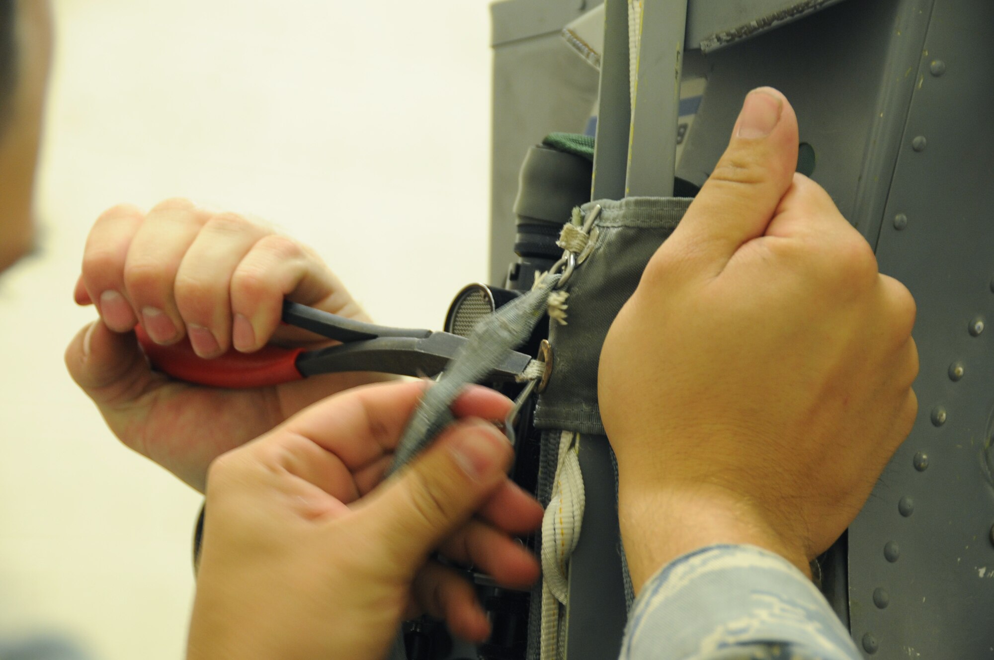 Senior Airman Josh Mertz, 28th Maintenance Squadron aircrew egress systems journeyman, installs an arm strap assembly on an advanced concept ejection seat II, while Staff Sgt. Don Mings, 28th Maintenance Squadron aircrew egress systems journeyman, holds the strap in place with pliers here, August 27.  Airman Mertz is threading an arm strap deployment lanyard through the ACES II. (U.S Air Force photo/Airman 1st Class Anthony Sanchelli)