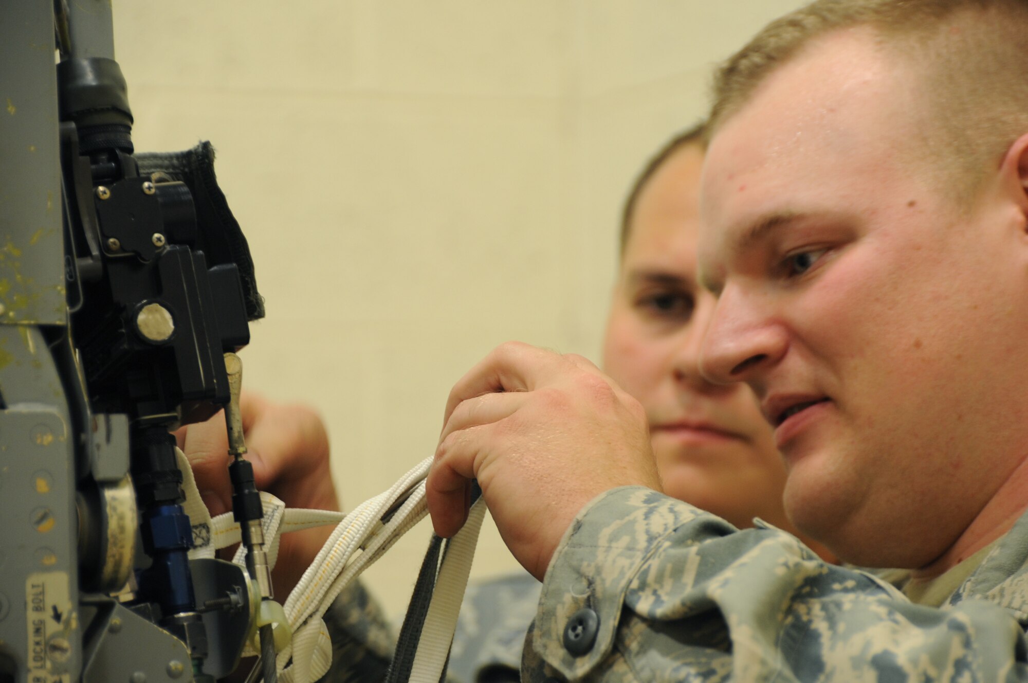 Senior Airman Josh Mertz, 28th Maintenance Squadron aircrew egress systems journeyman, installs an arm strap assembly on an advanced concept ejection seat II here, August 27.  Airman Mertz threads an arm strap deployment lanyard through the ACES II. (U.S Air Force photo/Airman 1st Class Anthony Sanchelli)