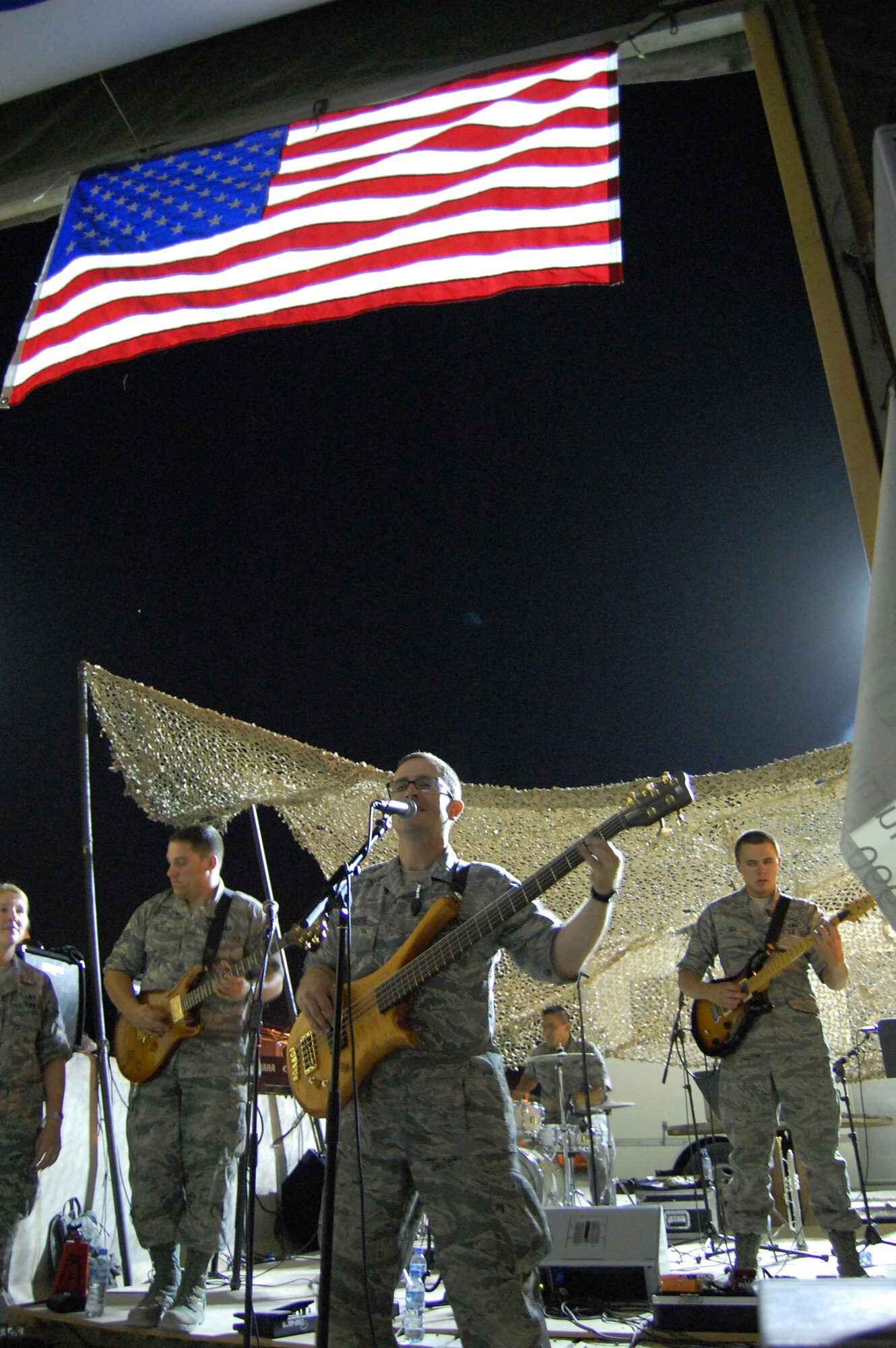 SOUTHWEST ASIA - Tech. Sgt. David Rochte of the AFCENT Band MOJAVE belts out a classic Rock favorite as 'Old Glory' blows freely above in the hot desert wind.   The Camelot Officer's Club,here, hosted an "All Ranks Night" where MOJAVE treated the standing-room-only crowd to an energizing mix of new and old Rock to support the efforts of U.S. and Coalition service members. The AFCENT Band MOJAVE consists of Airmen from the Ohio Air National Guard Band of the Great Lakes. (U.S. Air Force photo/Staff Sgt. Nicholas Kuetemeyer) 