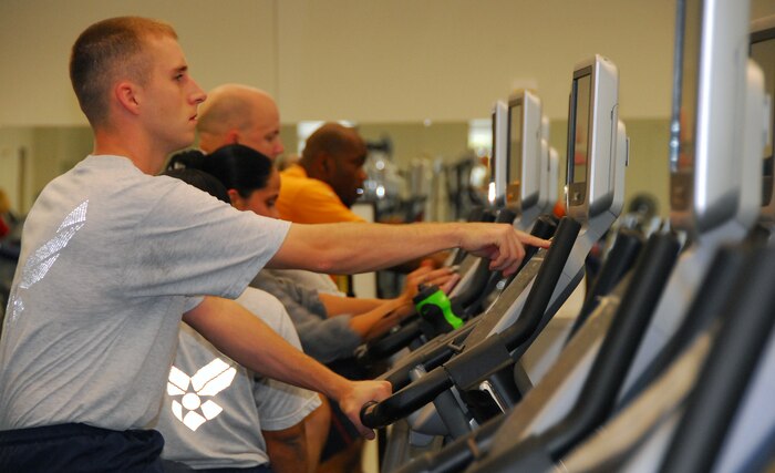 Staff Sgt. Joshua Cox switches stations to watch a college football game while working out on a stationary bicycle at the Fitness and Sports Center here Nov. 30. Sergeant Cox performs individual physical training prior to leading trainees from the 373rd Training Squadron in unit physical training to ensure he is fit and able to lead the unit's training program. Sergeant Cox is a military training leader with the 373rd Training Squadron. (U.S. Air Force photo/Staff Sgt. Daniel Bowles)