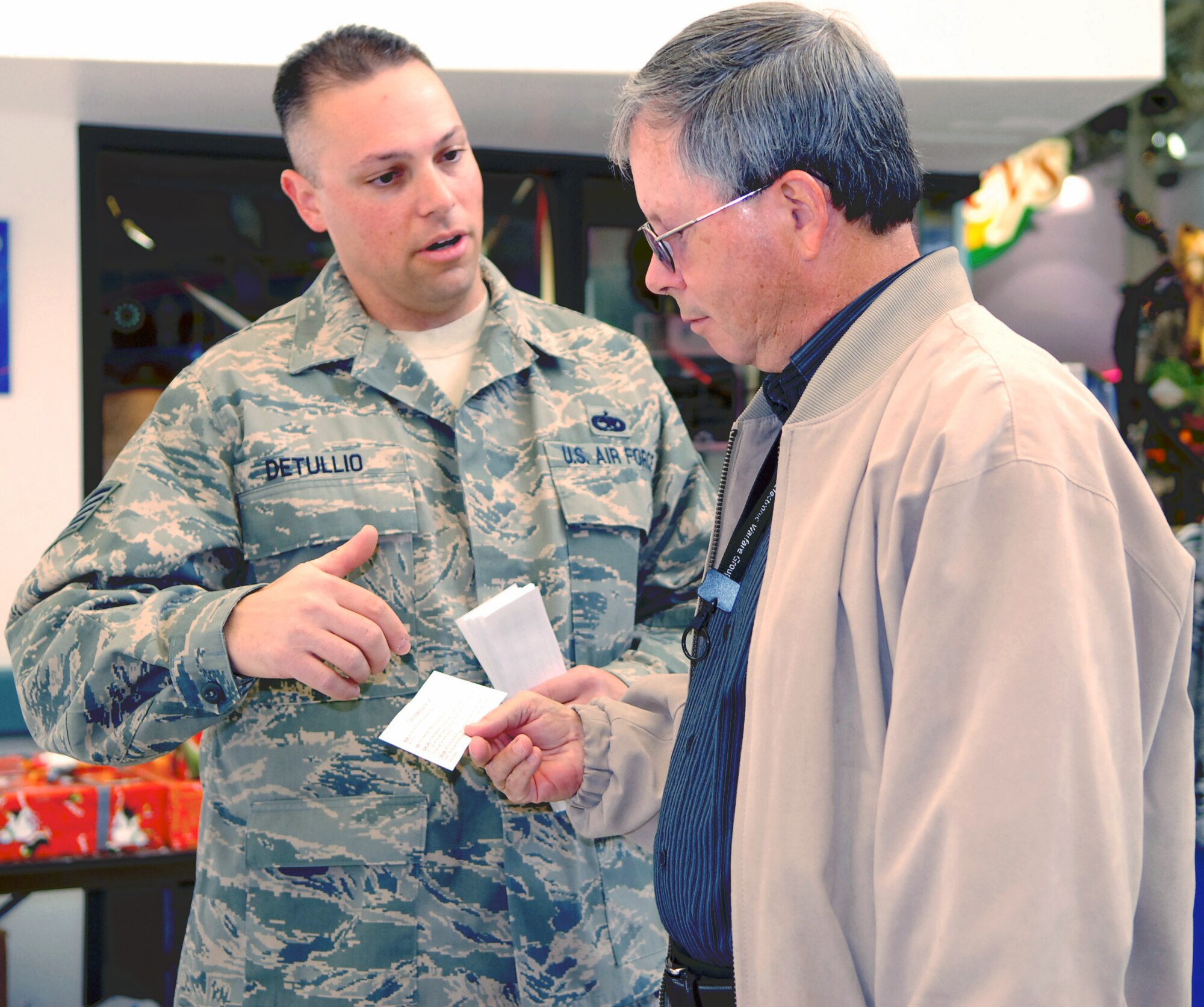 Tech. Sgt. Jason DeTullio, 412th Maintenance Group unit deployment officer, explains the purpose of the Operation Touch Our Warriors donation list to a Base Exchange shopper. Operation Touch Our Warriors is a yearly event that provides donated gifts to Edwards personnel who are deployed during the holiday season. (Air Force photo/2nd Lt Belena Marquez)