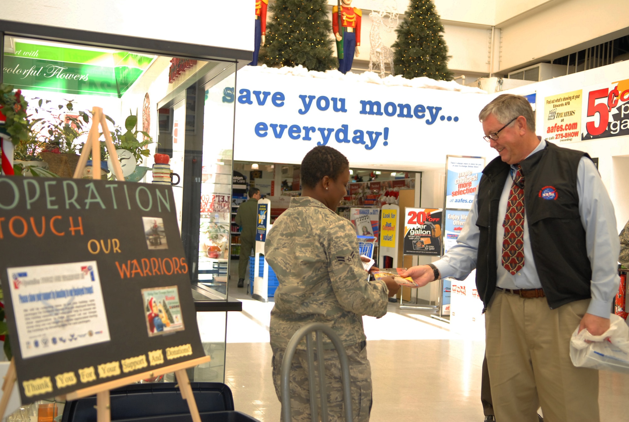 Airman 1st Class Kafilat Jinadu, 412th Test Wing executive assistant, accepts a donation from Chauncey Williams, National Aeronautics and Space Administration attorney, for Operation Touch Our Warriors.  Operation Touch Our Warriors is a yearly event that provides donated gifts to Edwards personnel who are deployed during the holiday season. (Air Force photo/2nd Lt Belena Marquez)