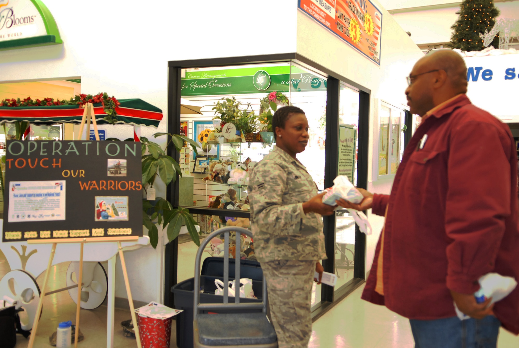 Airman 1st Class Kafilat Jinadu, 412th Test Wing executive assistant, accepts a donation from Oliver Edwards, 412th Aircraft Maintenance Squadron work supervisor, for Operation Touch Our Warriors.  Operation Touch Our Warriors is a yearly event that provides donated gifts to Edwards personnel who are deployed during the holiday season. (Air Force photo/2nd Lt Belena Marquez)