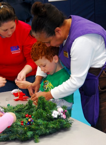 Denise Battle helps Evan Peirce ring in the holiday season by decorating a holiday wreath at the Youth Programs Center here Dec. 1. Children, childcare workers and volunteers gathered at the center to make wreaths for donation to the Festival of Wreaths and the Medical University of South Carolina Children's Hospital. Ms. Battle is a supervisor with the Child Development Center and Evan is the son of Master Sgt. Robert Peirce who is with the 437th Comptroller Squadron. (U.S. Air Force photo/Staff Sgt. Daniel Bowles)