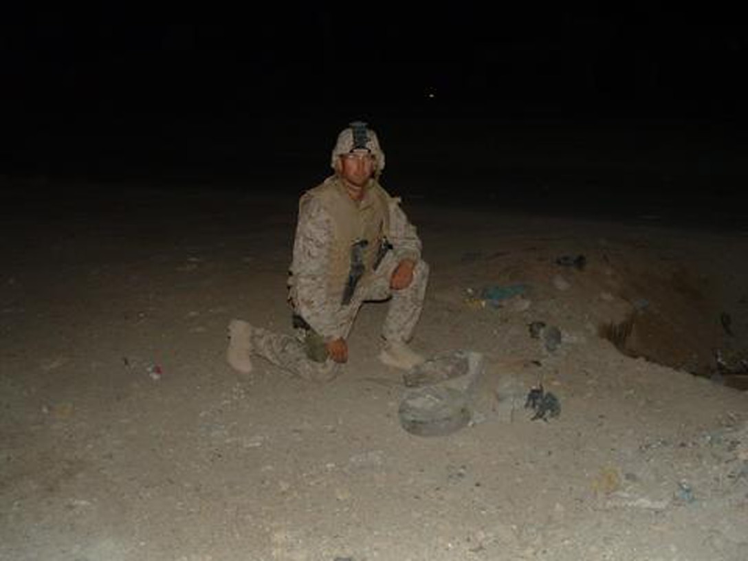 Gunnery Sgt. Michael Burghardt kneels next to two land mines that were cemented together to form an Improvised Explosive Device.  Burghardt was awarded the Bronze Star with combat distinguishing device for his actions as the Explosive Ordnance Disposal team leader while in Iraq. (Photo courtesy of Gunnery Sgt. Michael Burghardt)