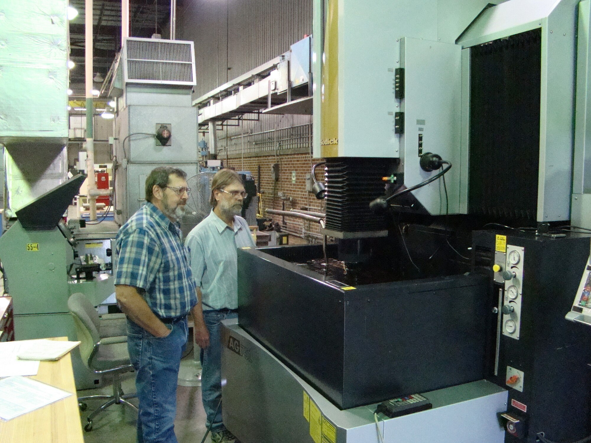 Designer Scott Wieland and Machinist Bill Hopkins observe a new electric discharge machining in operation at the Arnold Engineering Development Center Model Shop as it is being used to produce balances used in the center's 16-foot transonic wind tunnel. (Photo by Bob Boswell)