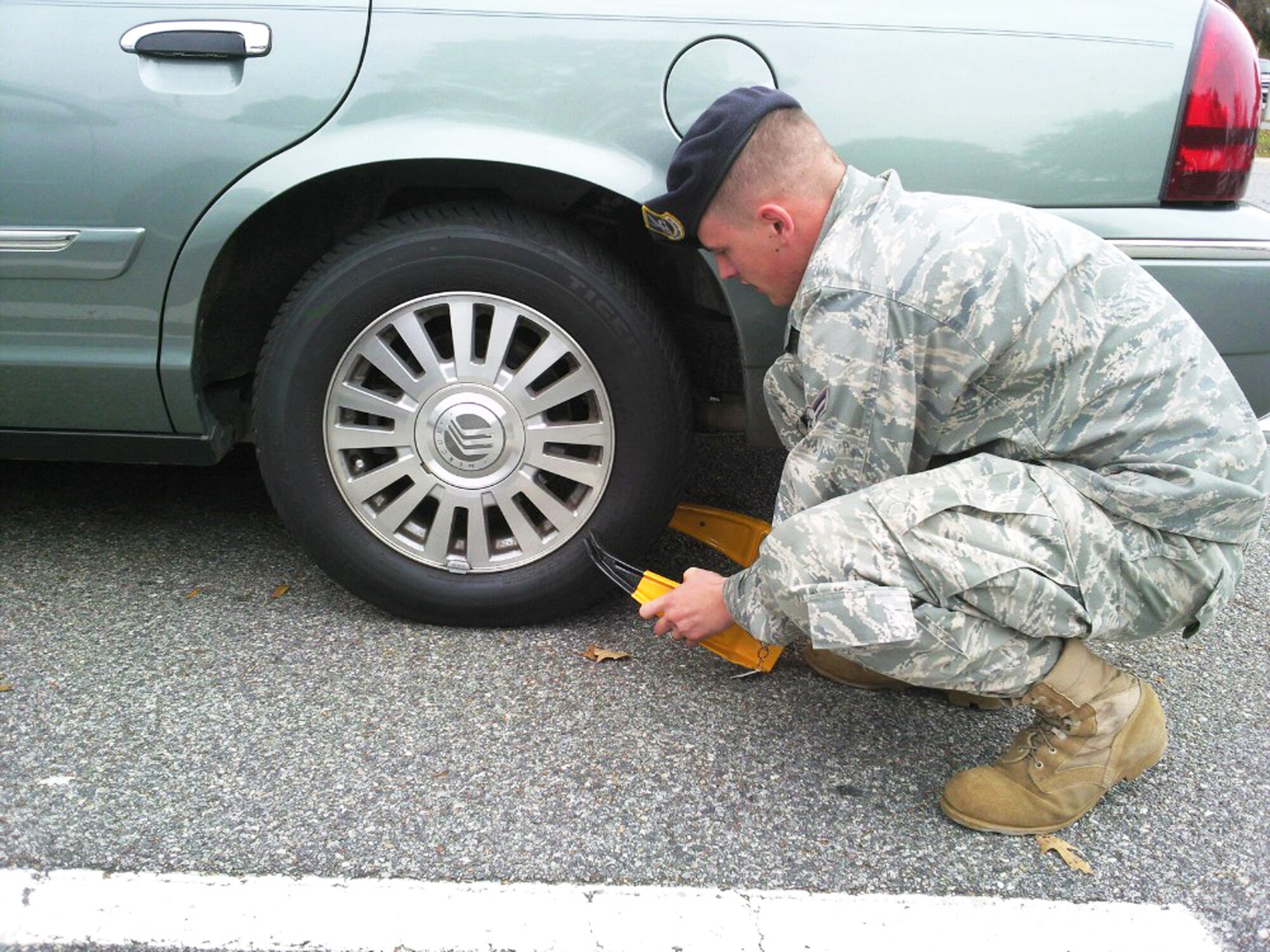 A1C John Duffin, 78th SFS, attaches a vehicle immobilization boot to a car. The 78th Security Forces Squadron is ramping up its enforcement efforts by assigning parking wardens to patrol parking lots and attaching vehicle immobilization boots on cars found violating parking policies. U. S. Air Force photo by SSgt. Angelo Corbin