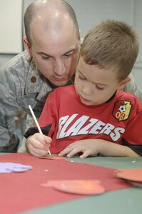 Maj. Tim Houle looks on as his son Adrien Houle decorates a holiday ornament at the Holiday Tree Lighting ceremony at the Youth Programs Center here Dec. 2. Charleston AFB hosted the annual event which included naming the Holiday Greeting Card Contest award winners for first place, 315th Maintenance Squadron, second place, 437th Medical Group, and third place, 437th Security Forces Squadron. Major Houle is a physician assistant assigned to the 437 MDG. (U.S. Air Force photo/Airman 1st Class Lauren Laidlaw)