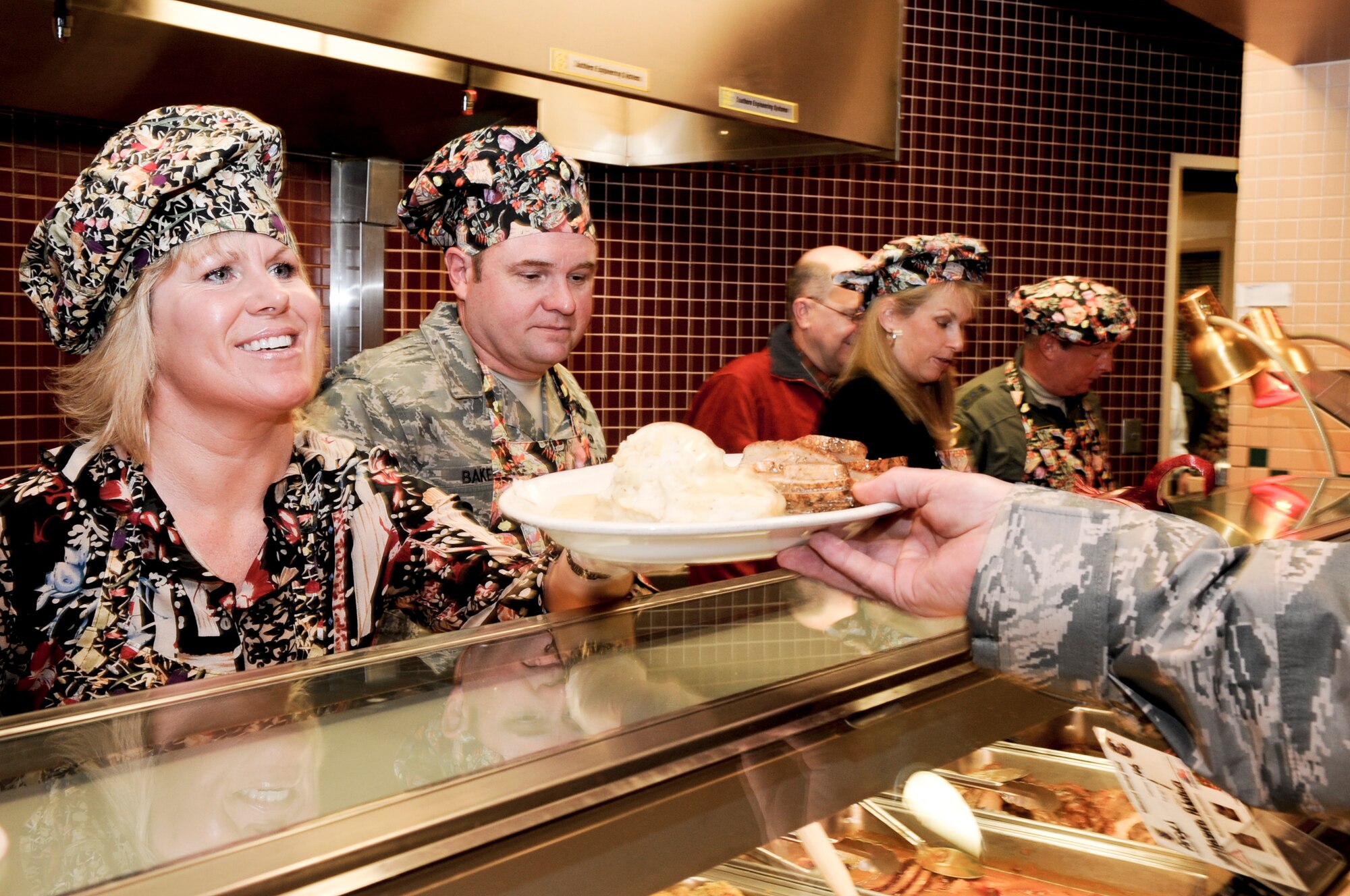 ELMENDORF AIR FORCE BASE, Alaska -- Peggy Baker hands a thanksgiving dinner to an airman at the Iditarod Dinning Facility. Baker was volunteering with her husband Chief Master Sgt. Tom Baker, 3rd Wing Command Chief Master Sergeant, Lt. Gen. Dana Atkins, commander of Alaskan Command, Alaskan North American Aerospace Defense Command Region, Joint Task Force Alaska and 11th Air Force, and his wife Laura Atkins. On Thanksgiving Day many commanding members of Elmendorf volunteered their holiday time to serve the airmen here. (U.S. Air Force photo/ Airman Jack Sanders)