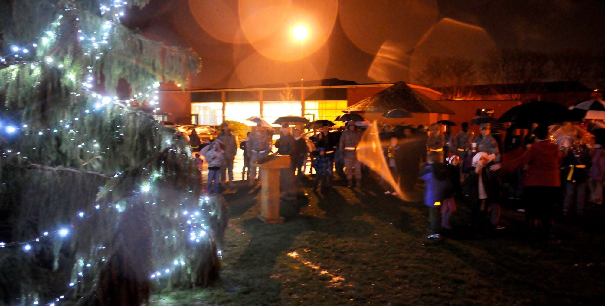 RAF MILDENHALL, England -- Military families and their children gather under umbrellas to hide from the rain as Col. Chad Manske, 100th Air Refueling Wing Commander, conducts the annual tree lighting ceremony Dec. 2.  The event included Christmas carols sung by children from the base youth center and a surprise visit from Santa.  (U.S. Air Force photo/Staff Sgt. Christopher L. Ingersoll)