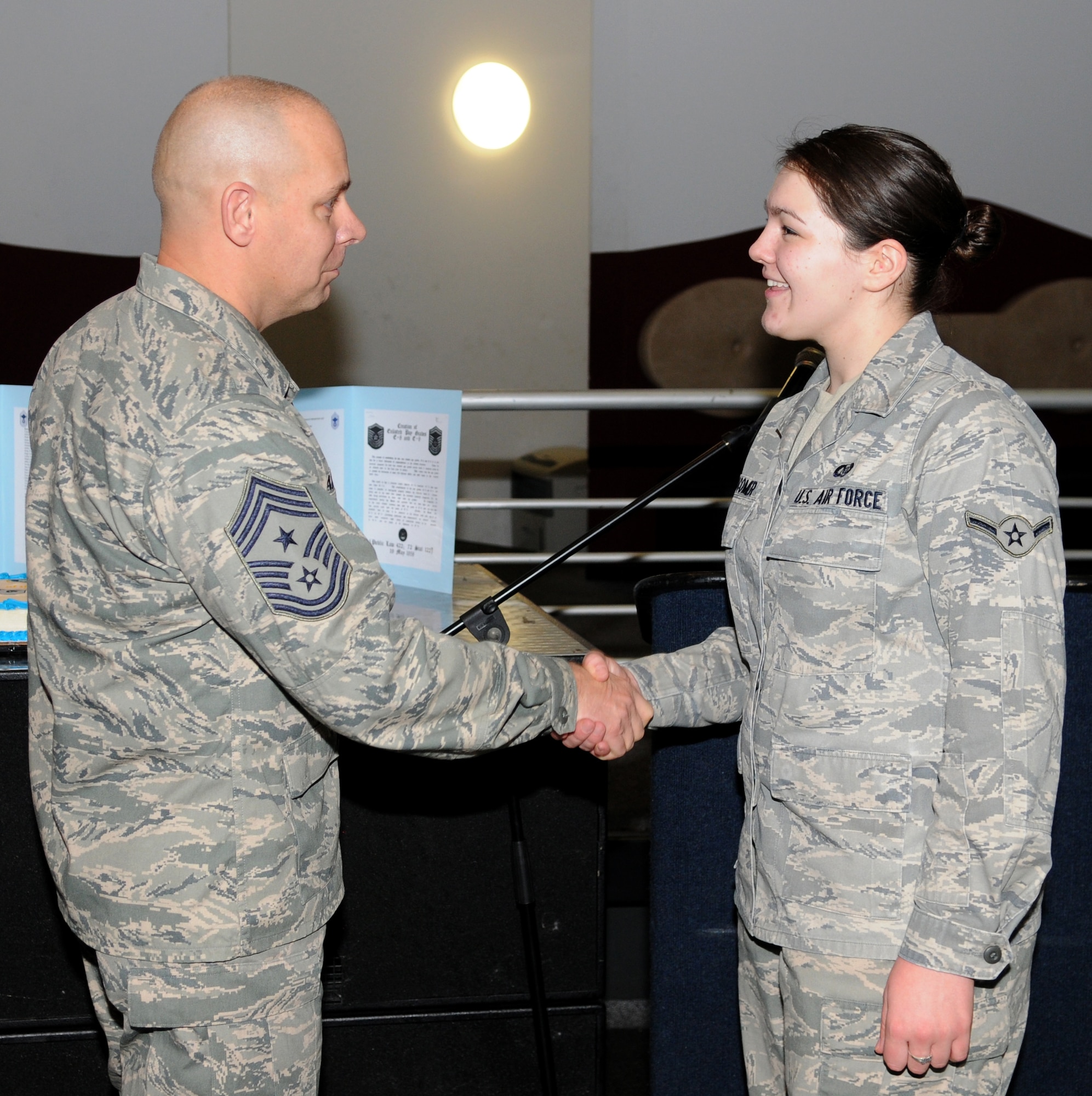 Chief Master Sgt. Dennis Vannorsdall, 3rd Air Force Command Chief thanks Airman Emma R. Newcomer, Air Tasking Order Production Technician, 603rd Air and Space Operations Center for leading the audience in the Airman's Creed during the 50th anniversary of the chief master sergeant rank celebration, sponsored by the Ramstein Area Chiefs Group at the enlisted club Dec. 1. (U.S. Air Force photo by Airman 1st Class Caleb Pierce)