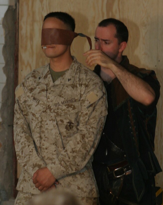 CAMP BLUE DIAMOND, AR RAMADI, Iraq - "Slash" Spencer Humm of the 'Shakespearean comic-sword fighting duo,' Hack and Slash, blindfolds 20-year-old Lance Cpl. Jason E. Myer during a trick where Myer will think they knocked half a cigarette from his lips with a whip while blindfolded during Operation Swashbuckle. Hack and Slash presented the four-man comedy show that provided an explosive round of entertainment for more than 100 Marines, sailors and soldiers here serving with the 2nd Marine Division in support of Operation Iraqi Freedom.