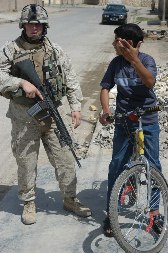AR RAMADI, Iraq (April 11, 2005) - Corporal Michael J. Kelly, a team leader with 2nd Squad, 1st Platoon, Company A, 1st Battalion, 5th Marine Regiment, questions an Iraqi boy on a bicycle why he's following his squad. The boy followed Marines with 2nd Squad, 1st Platoon, Company A, 1st Battalion, 5th Marines, for more than 20 minutes as they conducted a patrol through the streets here. The boy also changed close in an effort to disguise himself, but Kelly, a 22-year-old Boston native, wasn't fooled. Kelly questioned the boy because of his suspicious activity. Photo by Cpl. Tom Sloan