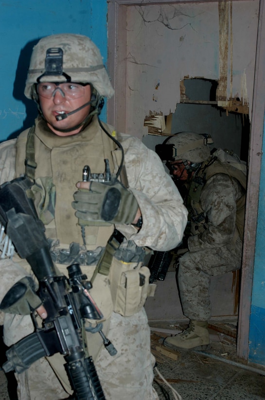 AR RAMADI Iraq (July 5, 2005) - Corporal Brett J. Springer, a TOW gunner and section leader for 1st Section, 2nd Platoon, Company W, 1st Battalion, 5th Marine Regiment, communicates with fellow Marines on his radio after busting through a locked door in a building here in the city during a mission July 5. His comrade, Cpl. Dennis J. Jackson, a machine gunner with 1st Section, and 23-year-old Manhattan, Kan., native, follows close behind. The 28-year-old Springer from Kearney, Neb., and Marines with 2nd Platoon conducted a proactive operation to encourage Ar Ramadi citizens to move their trashcans off the streets and place them in the yards and behind their homes. The Iraqi government recently distributed new, orange, industrial-sized trash containers throughout the city for citizens to use to clean up rubbish, but Marine officials with the 1st Battalion, 5th Marines suspect insurgents will exploit them for terror and place improvised explosive devices in them. Photo by Cpl. Tom Sloan