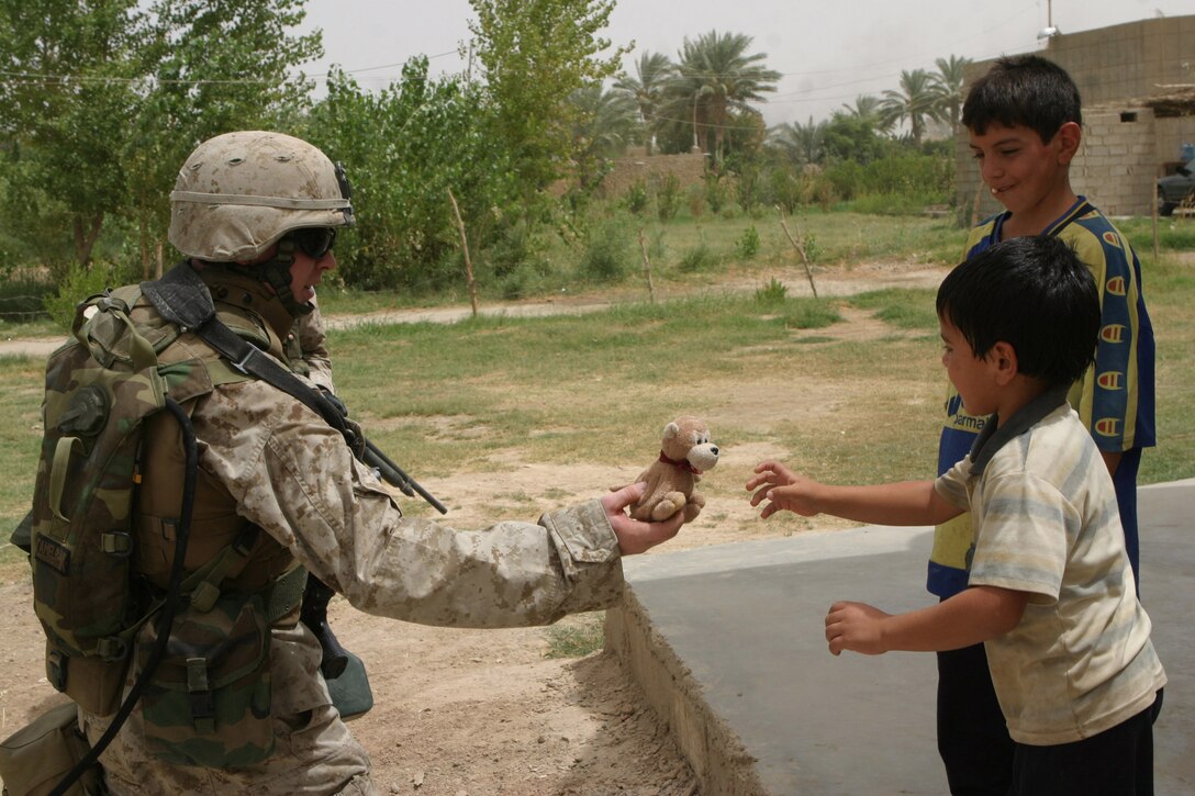 CAMP BLUE DIAMOND, AR RAMADI, Iraq - Corporal William Bryan Malin, a Squad Automatic Weapon machine gunner with the camp's guard force, hands a stuffed animal to an Iraqi child while on patrol outside of the camp's walls.  He revels in his ability to be able to do something positive for the children here.  For the past six months, the 20-year-old Colorado Springs, Colo. native and his squad have been patrolling through the farm lands and villages that cushion the outside walls of the camp.  The children know who he is, because they usually get a little teddy bear when he passes through their field.  U.S. Marine Corps photo by Sgt. Stephen D'Alessio (RELEASED)