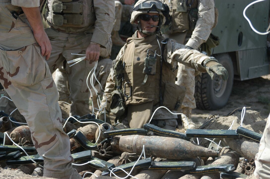 AR RAMADI, Iraq (Aug. 15, 2005) -Gunnery Sgt. John Kelsch, platoon sergeant for 4th Platoon, Company A, 1st Combat Engineer Battalion, which is in direct support of 1st Battalion, 5th Marine Regiment, points to a spot on a large weapons caches where C-4 explosives needs to be placed during a mission Aug. 15. Kelsch and other combat engineer conducted a weapons caches sweep through several acres of farmland located on the southern outskirts of the city here and uncovered several large weapons caches while supporting Operation Bullard II. First Battalion, Fifth Marines carried out the operation, which started before daylight and lasted until midday, in and around a small community on the edge of volatile Ramadi in an effort to capture insurgents and weapons. Combat engineer Marines discovered a mortar tube, more than 200 artillery shells in sizes ranging from 60 mm to 155 mm, four .50 caliber machine gun barrels plus more than 2000 rounds of ammunition and approximately 1000 7.62 mm rounds, 600 of which were armor piercing. The engineer Marines consolidated the munitions into one large caches and destroyed it with a controlled detonation set off by C-4 explosives. Infantrymen with the battalion searched houses, vehicles and personnel and captured 14 insurgents. Photo by: Cpl. Tom Sloan