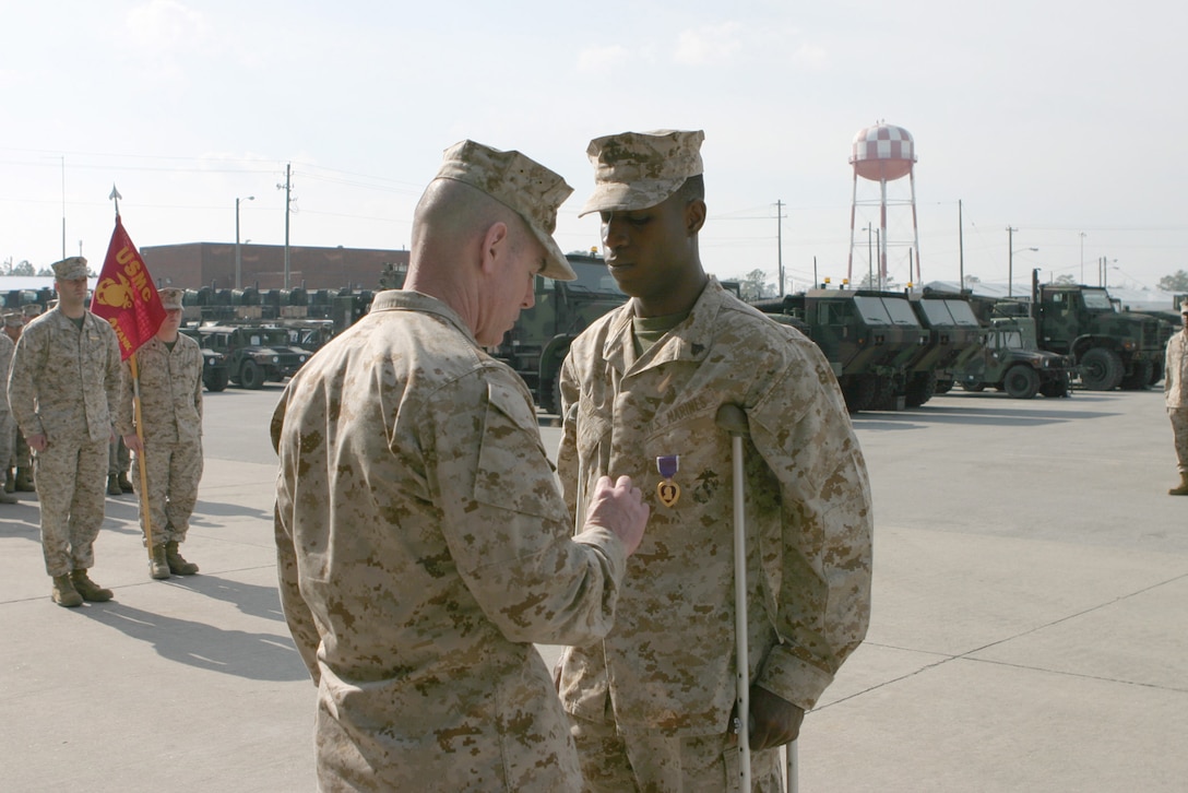 Corporal Richard C. Slew stands in a lot full of tanks with his Purple Heart award. Second Marine Division's Assistant Commander, Brig. Gen. Joseph J. McMenamin was on hand to present the award.  The Tampa, Fla. native's tank was hit by a rocket while patrolling the streets of Fallujah Nov. 10, 2004.  Slew survived the encounter with shrapnel wounds to his right foot.