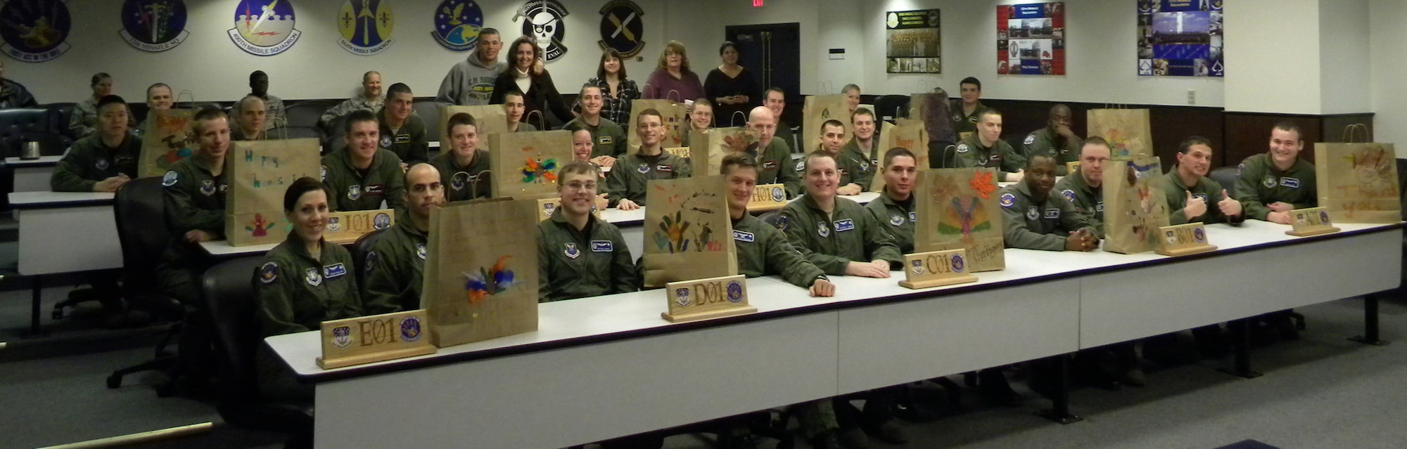 Missile crews and family members pose for a photo in the pre-departure room Thanksgiving morning prior to deploying for their holdiay shifts. Each two-person crew received a goodie bag with homemade treats to take with them on their holiday shift. (U.S. Air Force courtesy photo)