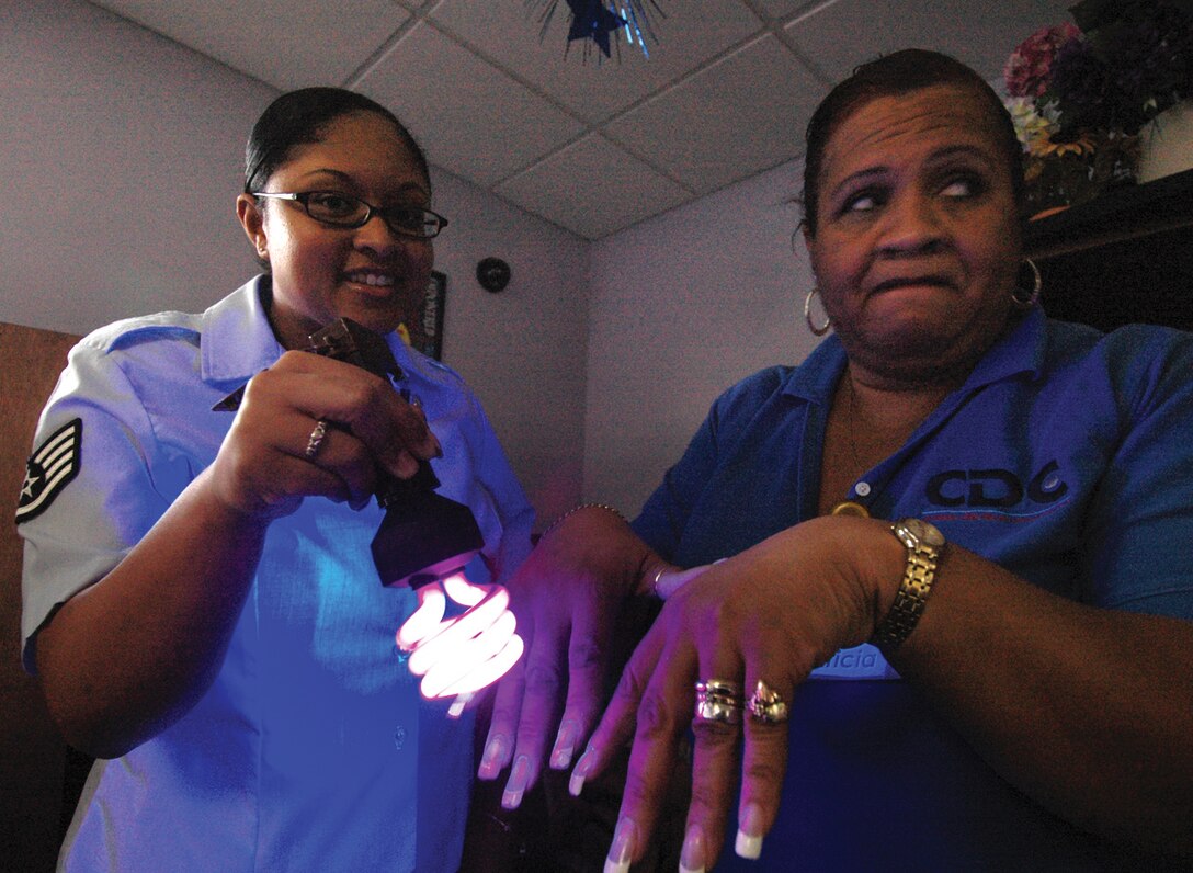 Staff Sgt. Danielle Costa, 779th Aerospace Medicine Squadron public health technician, scans the hands of Patricia Pitt, J.P. Hoyer Child Development Center III care giver, in semi-darkness under a black light to reveal possible germs left after washing her hands recently. Sergeant Costa briefed four different groups of child care givers at the J.P. Hoyer CDC to heighten their awareness on thorough handwashing. (U.S. Air Force photo/ Bobby Jones)