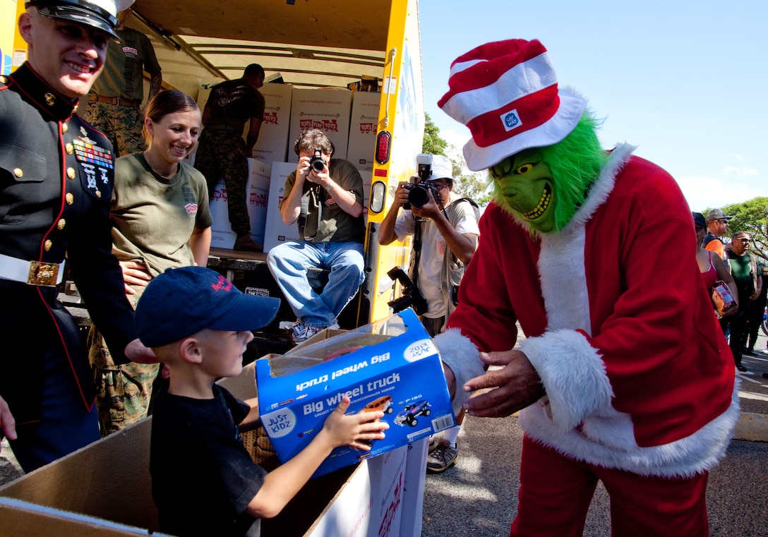 Eugene Legros, dressed as the Grinch, hands a toy to Zachary Crockett, son of Master Sgt. Scott Crockett, at the rally point for the 35th Annual Street Bikers United Toy Run Dec. 6. More than 6,500 moyorcyclists supported Toys for Tots on the ride from Ala Moana Beach Park to Kapiolani Community College here.
