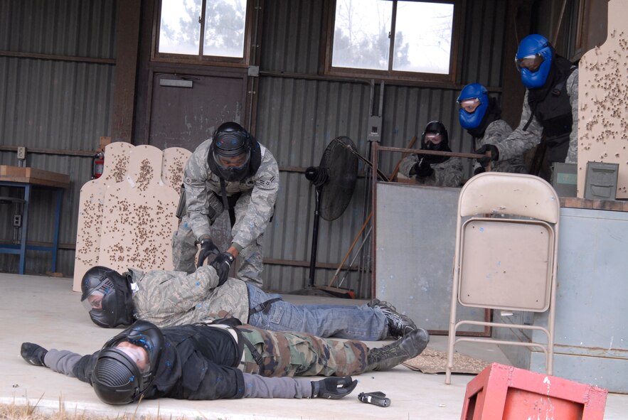 KUNSAN AIR BASE, Republic of Korea -- Airman 1st Class Tyrone Cooley, 8th Security Forces Squadron, handcuffs a downed opposing force member while Senior Airman Robert Davis, 8th Security Forces Squadron, provides cover during simulated rounds training here Dec. 2. The Simulated rounds training taught new Security Forces members proper ways to clear a building by engaging them with various situations. The instructors in blue helmets watched the scenario so they could go over the good and bad actions during the scenario brief at the conclusion. (U.S. Air Force photo/Staff Sgt. Darnell T. Cannady)